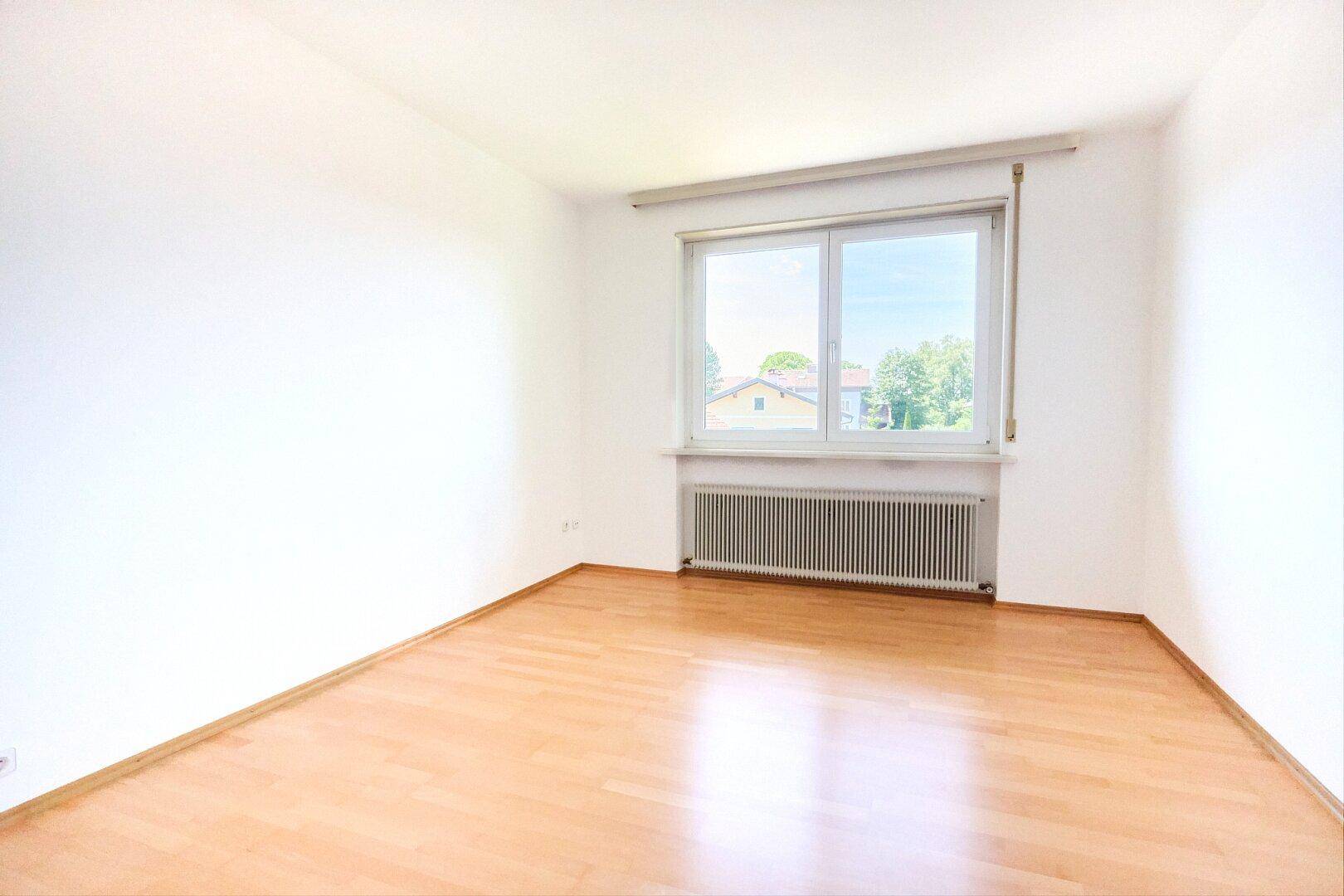 Leeres Zimmer mit hellem Holzboden, weißen Wänden und einem Fenster für natürliches Licht.