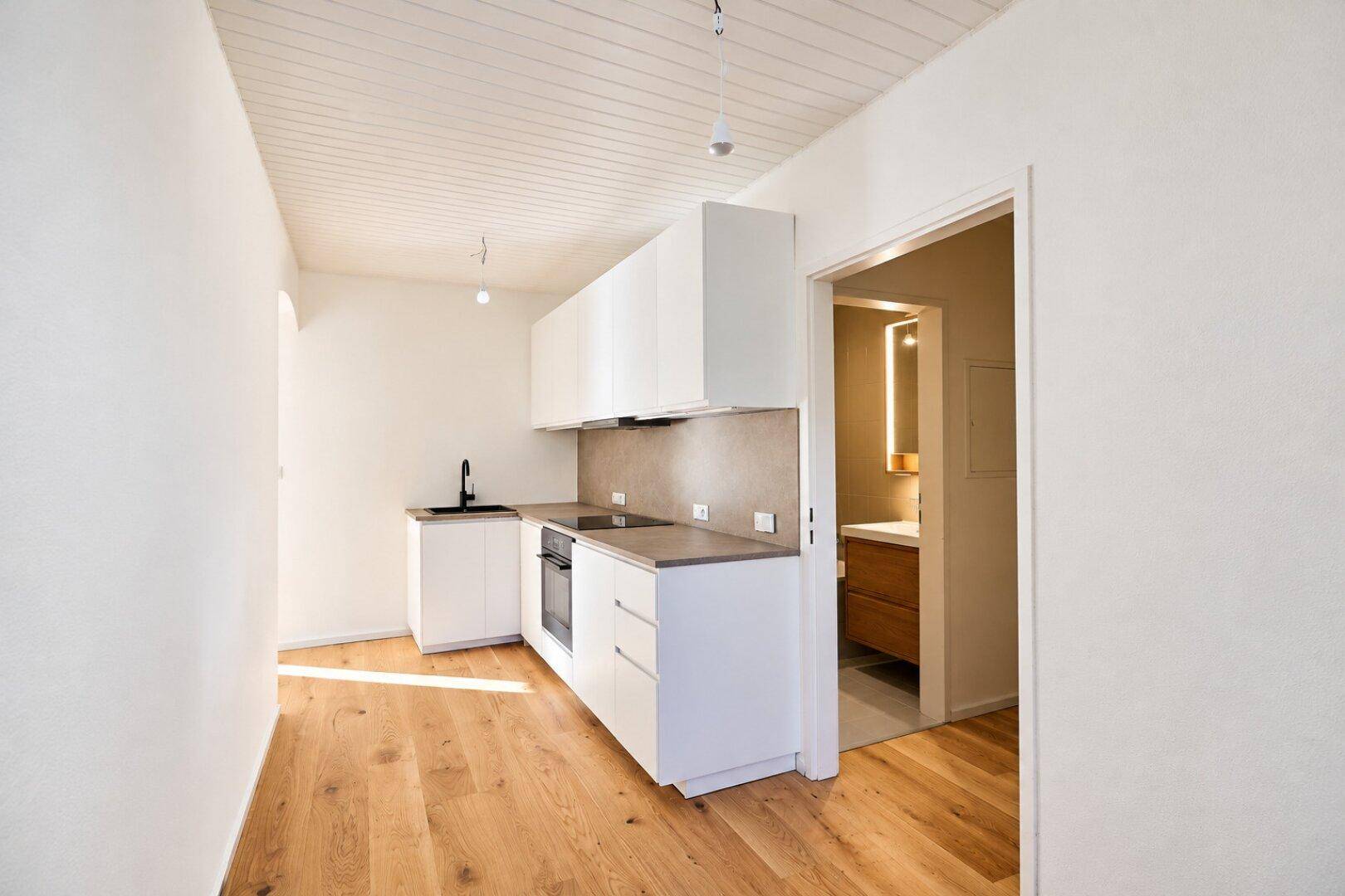 Moderne Küchenzeile mit weißen Schränken und Holzboden, angrenzend an ein Badezimmer.
