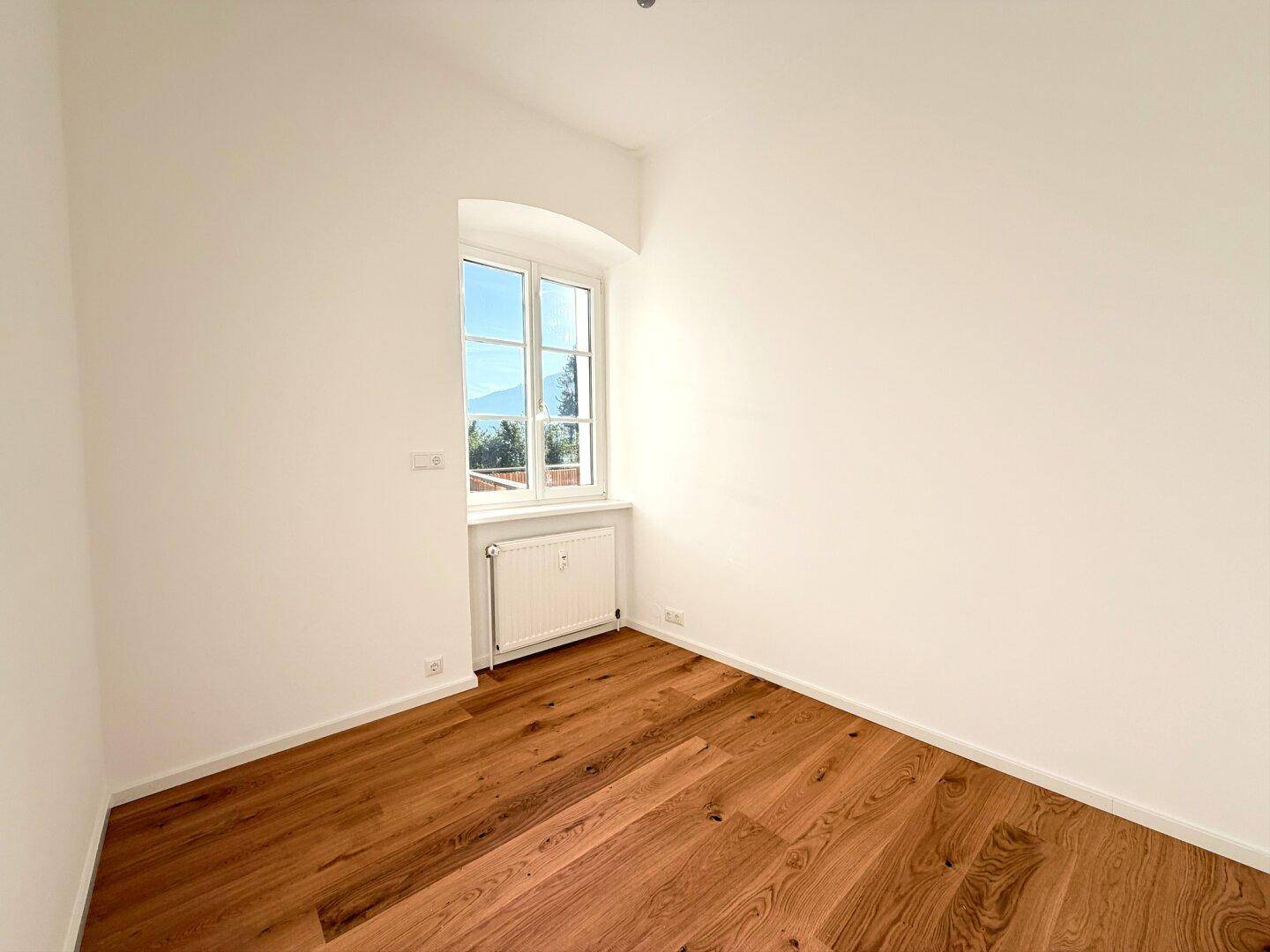 Helles Zimmer mit Holzboden und Fenster, das einen weiten Blick in die Landschaft bietet.