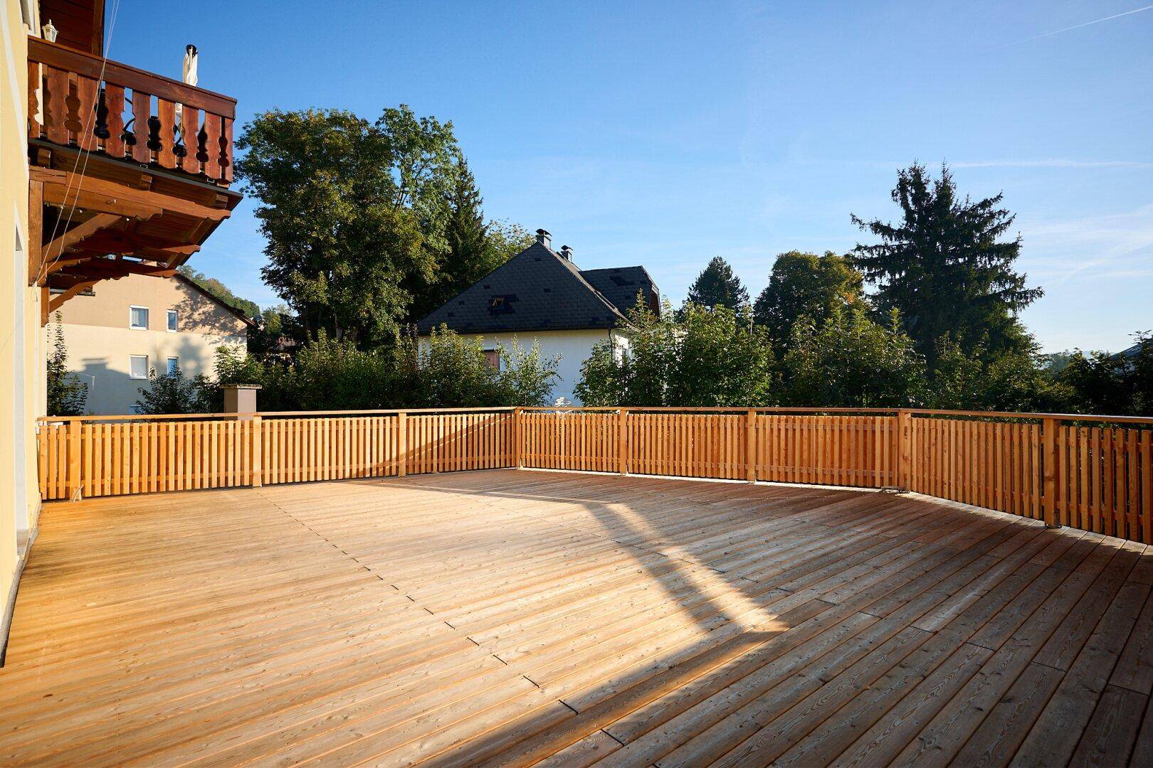Weitläufige Holzterrasse mit Holzzaun, umgeben von grüner Natur und Bäumen.