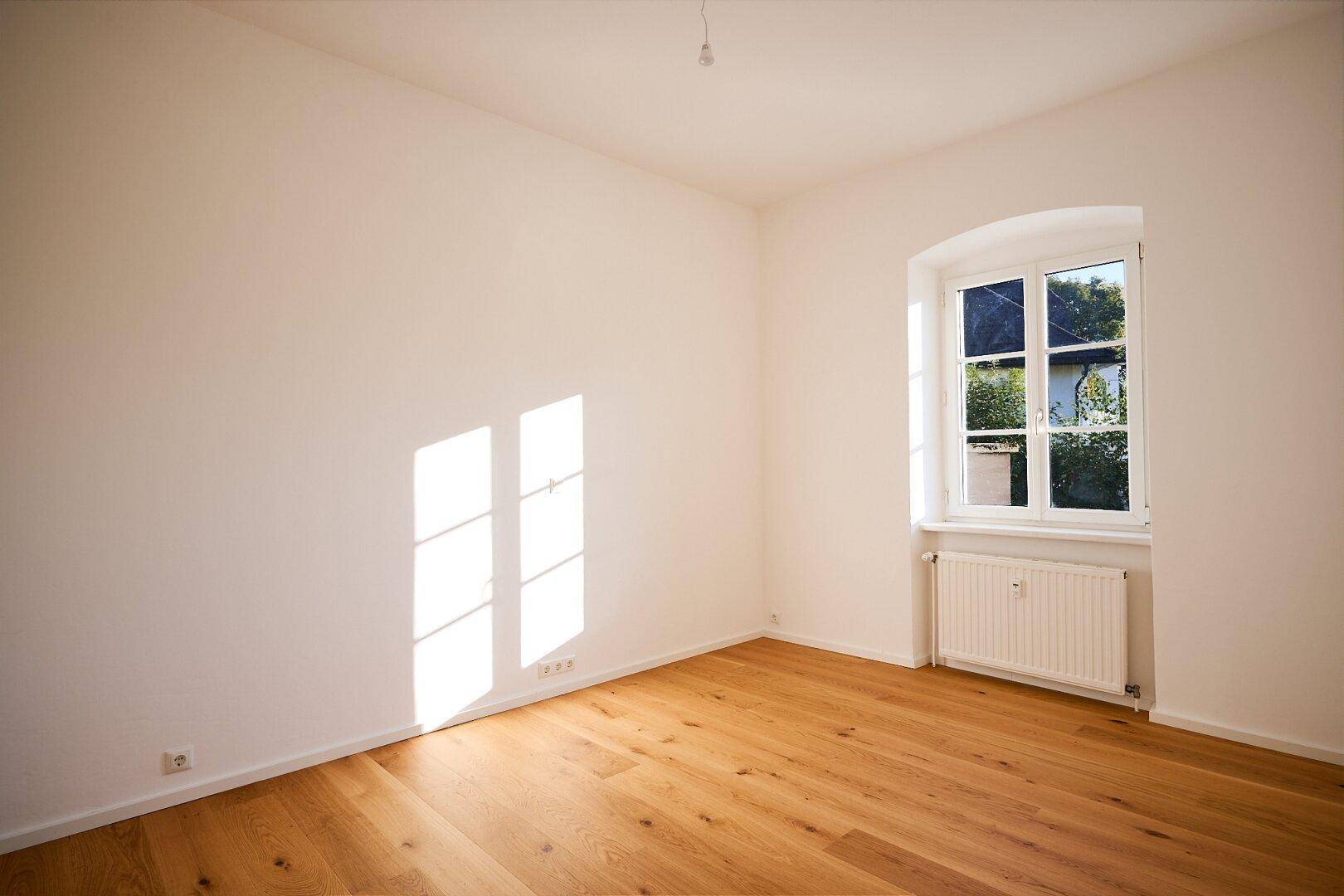 Gemütliches Zimmer mit Holzboden und einem Fenster, das viel Sonnenlicht hereinlässt.