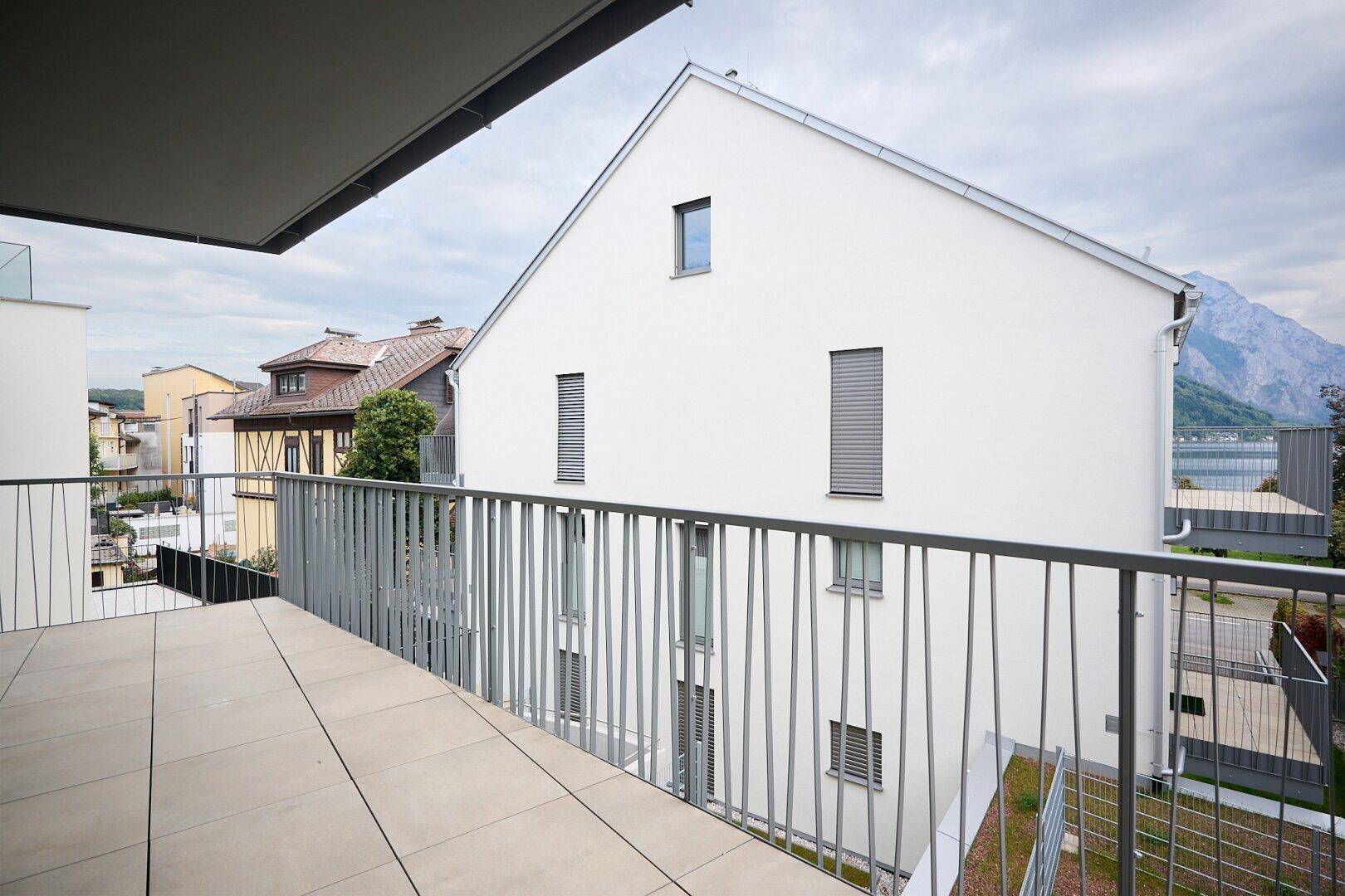 Geräumiger Balkon mit Fliesenboden und Blick auf die Berge und Nachbargebäude.