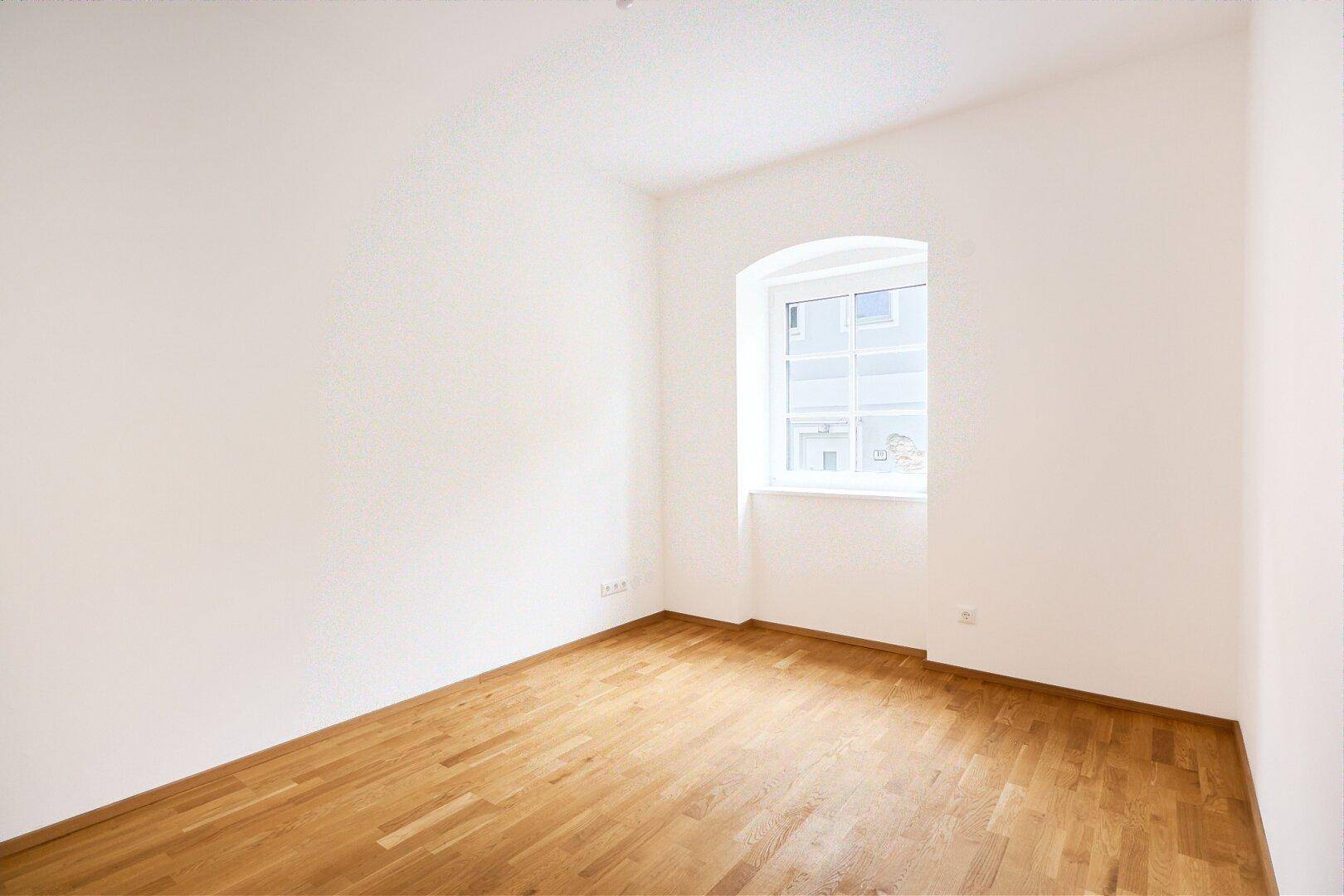 Ruhiges Zimmer mit Parkettboden und einem klassischen Bogenfenster.