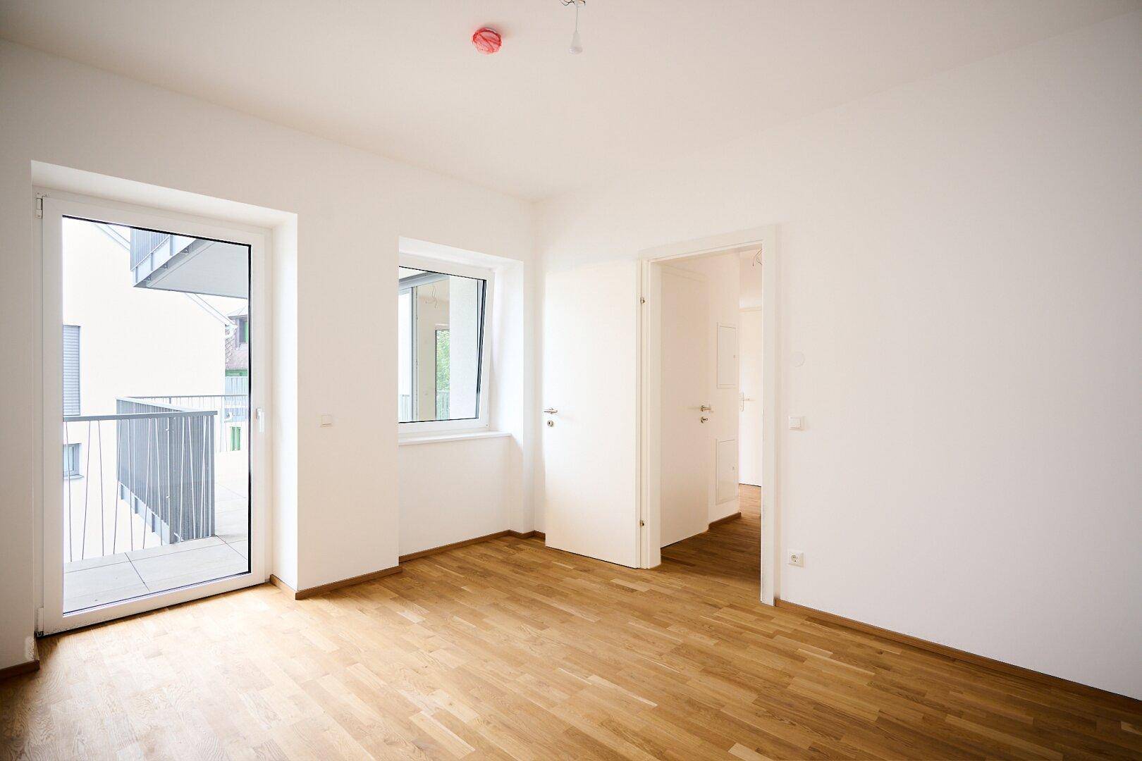 Helles Schlafzimmer mit Parkettboden und Zugang zu einem kleinen Balkon.