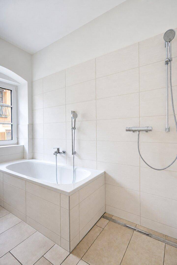 Modernes Badezimmer mit Badewanne, Duschbereich, Fenster und hellen Fliesen.