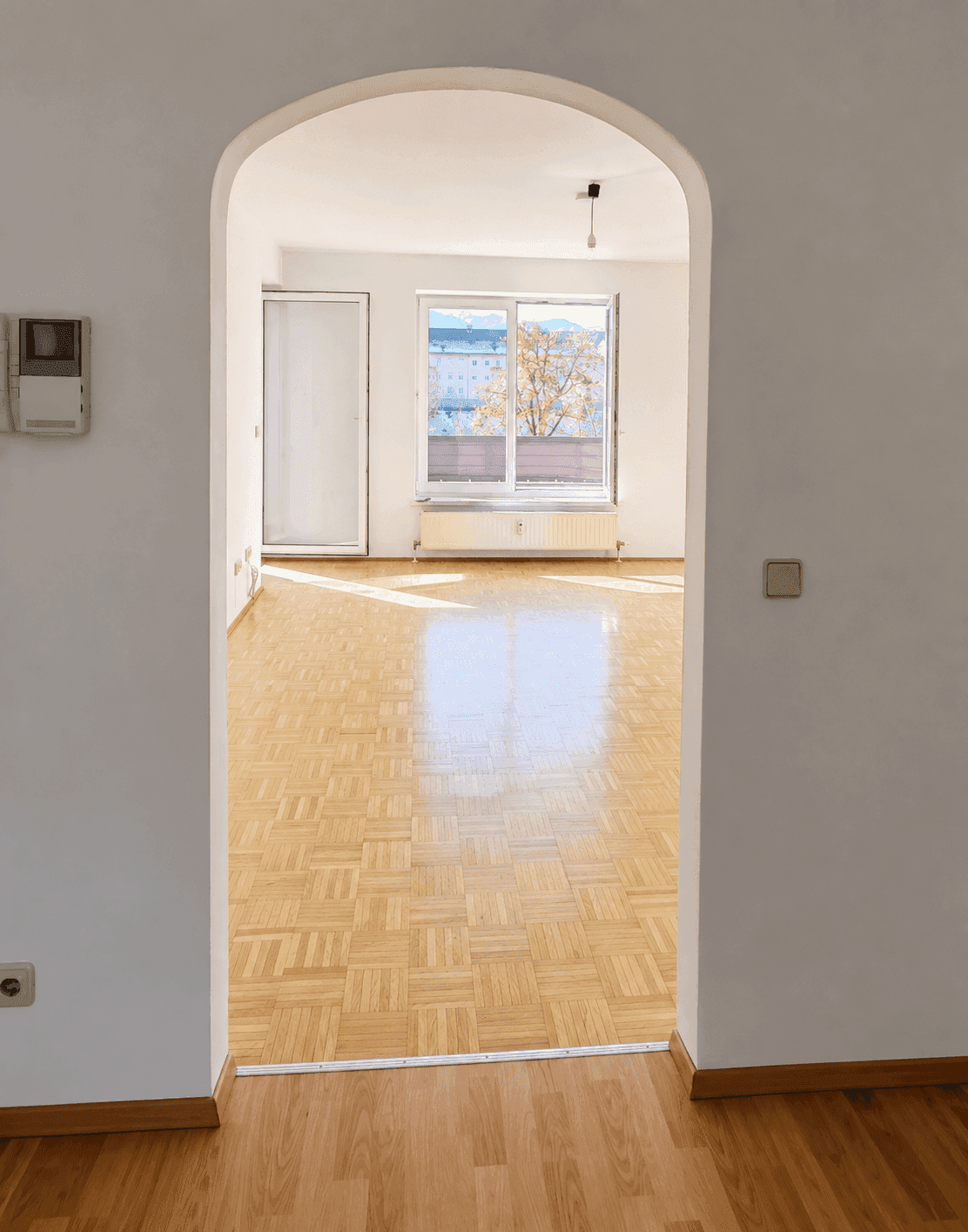 Blick durch einen eleganten Rundbogen in ein helles Zimmer mit glänzendem Parkettboden.