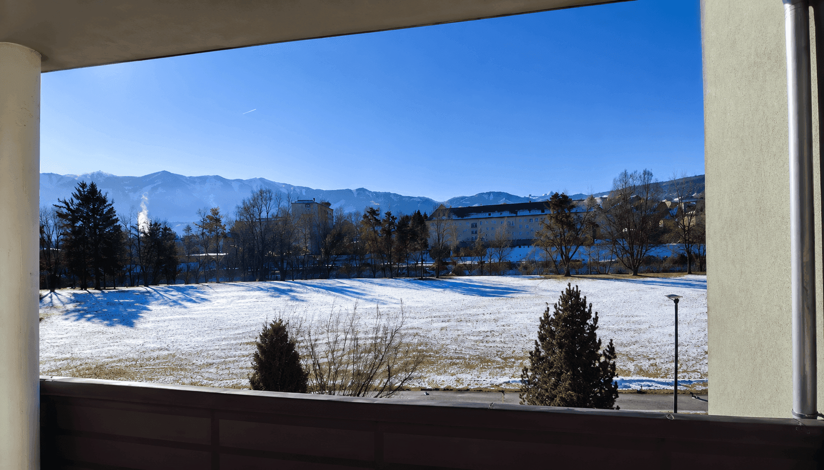 Winterlicher Ausblick vom Balkon auf schneebedeckte Felder und eine beeindruckende Bergkulisse.