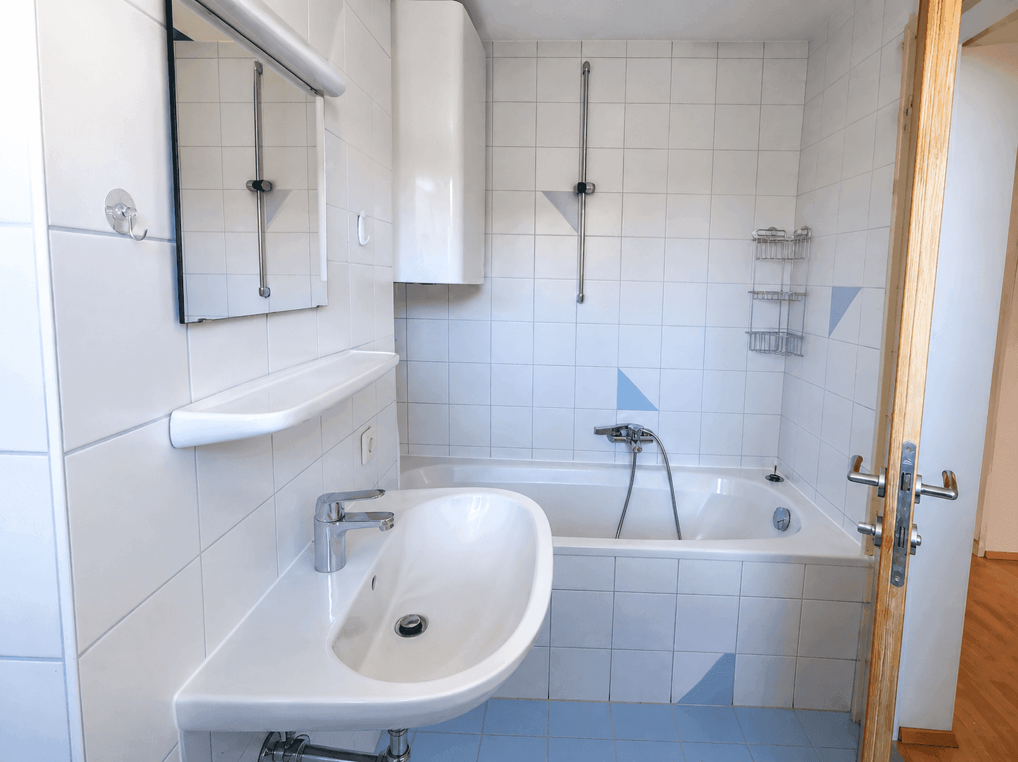 Badezimmer mit weißen Fliesen, blauem Boden, Einzelwaschbecken und einer Badewanne mit Duscharmatur.