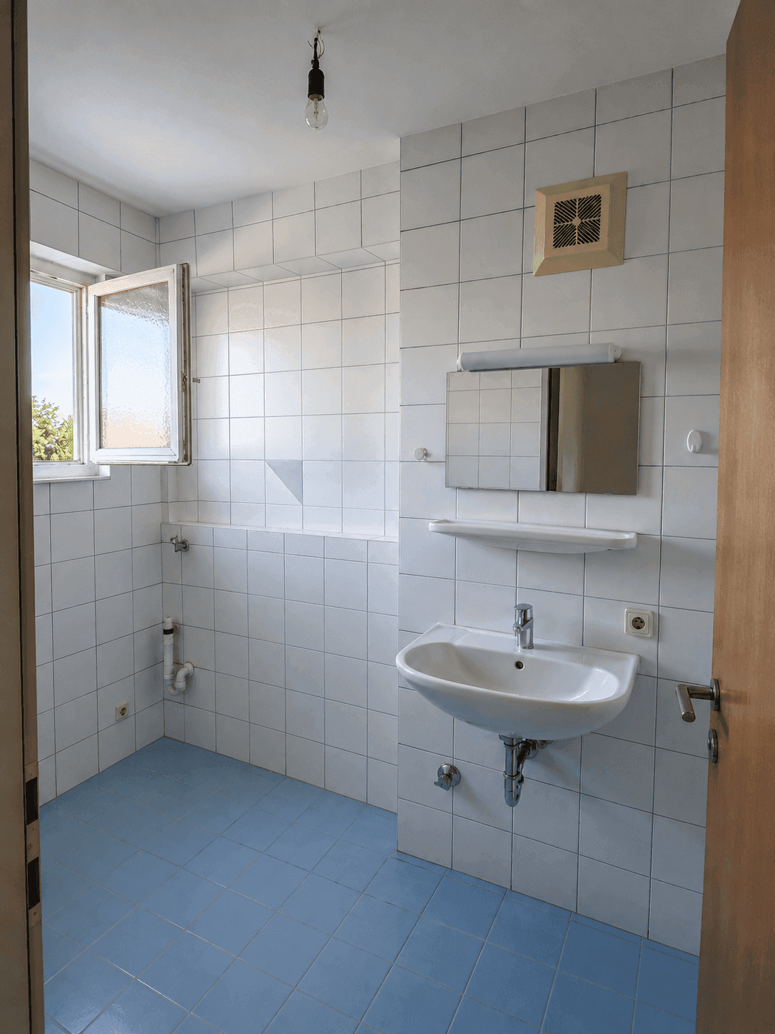 Badezimmer mit weißen Wandfliesen, blauem Boden, Einzelwaschbecken und einem Fenster für Tageslicht.