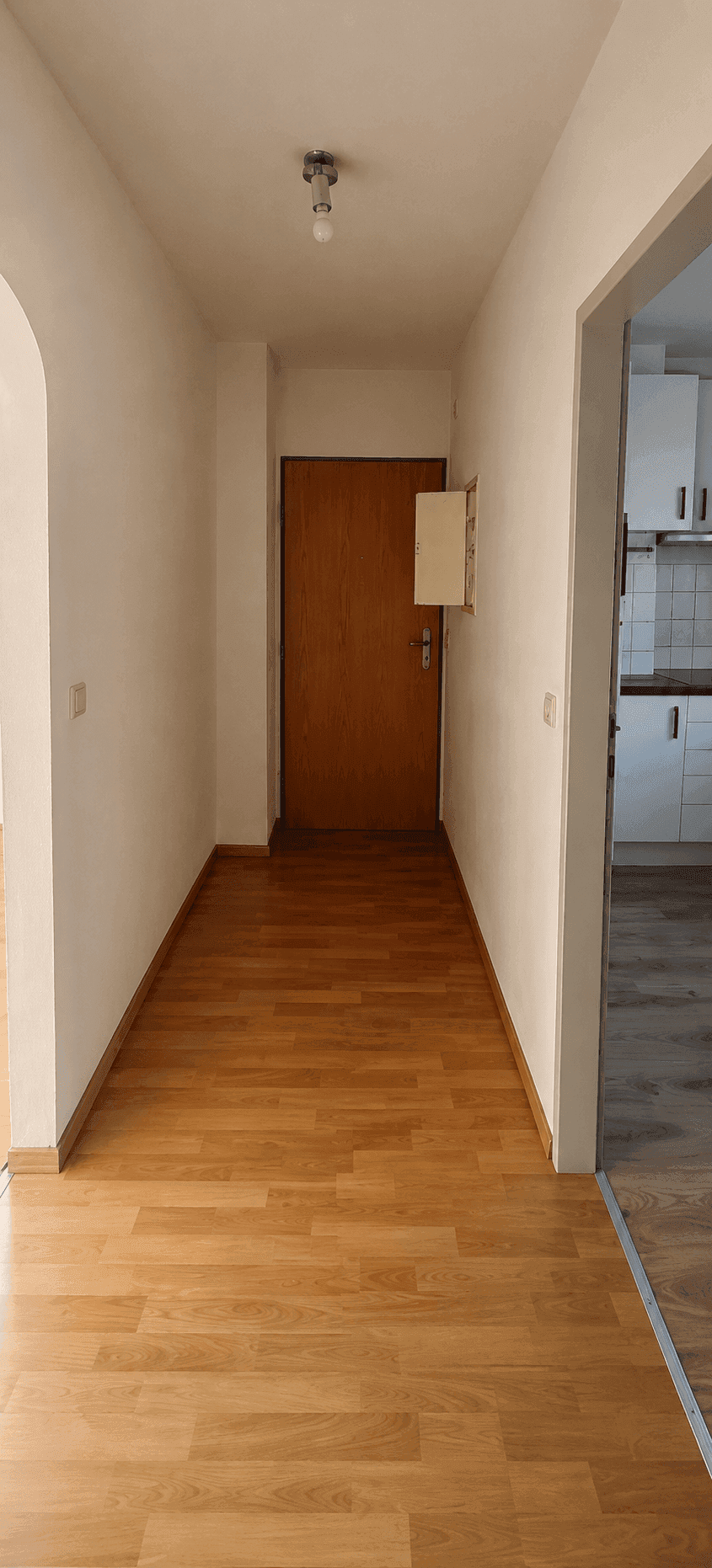 Heller Flur mit Laminatboden und Holztür, der einen Blick in die angrenzende Küche bietet.