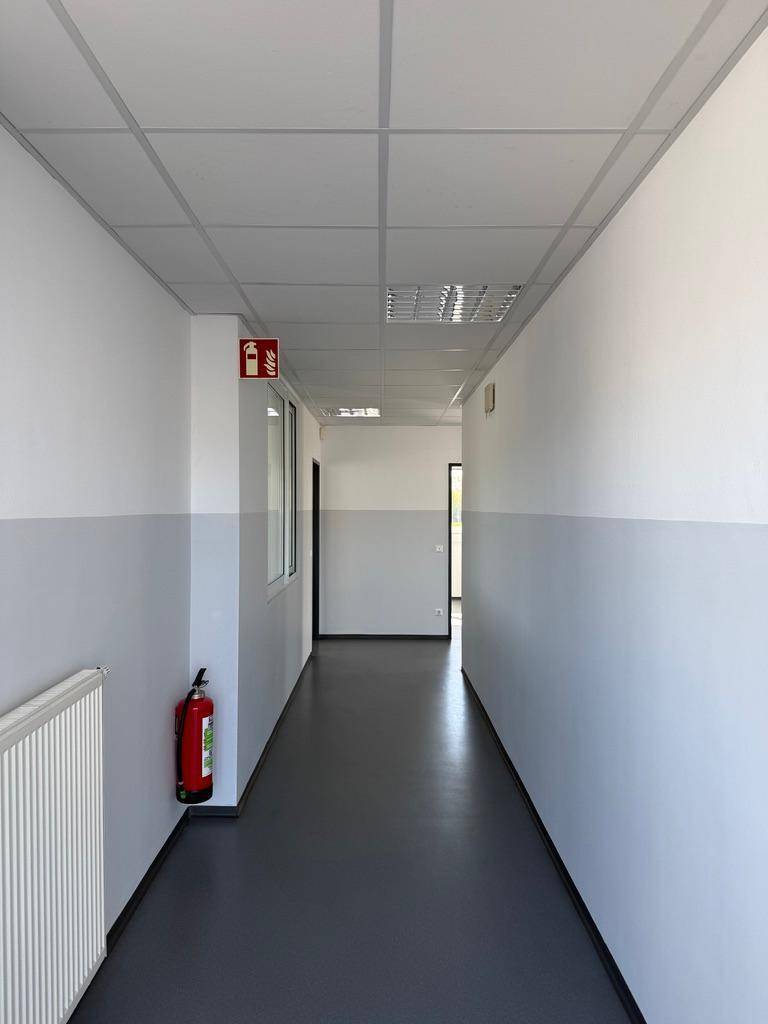 Langer, heller Flur mit weiß-grauen Wänden und einem Feuerlöscher an der Wand.
