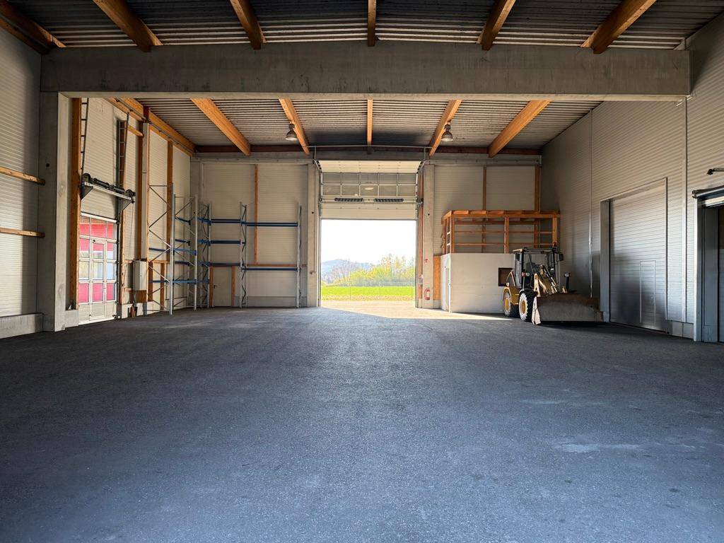 Geräumige Lagerhalle mit offenem Tor, das den Blick auf die grüne Landschaft freigibt.