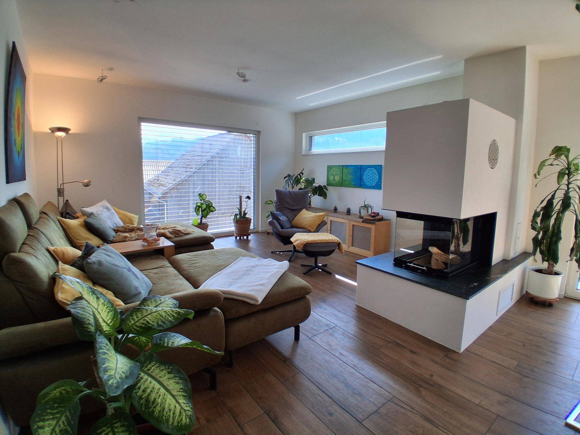 Helles Wohnzimmer mit gemütlichem Sofa, modernem Kamin und weitem Blick ins Grüne.