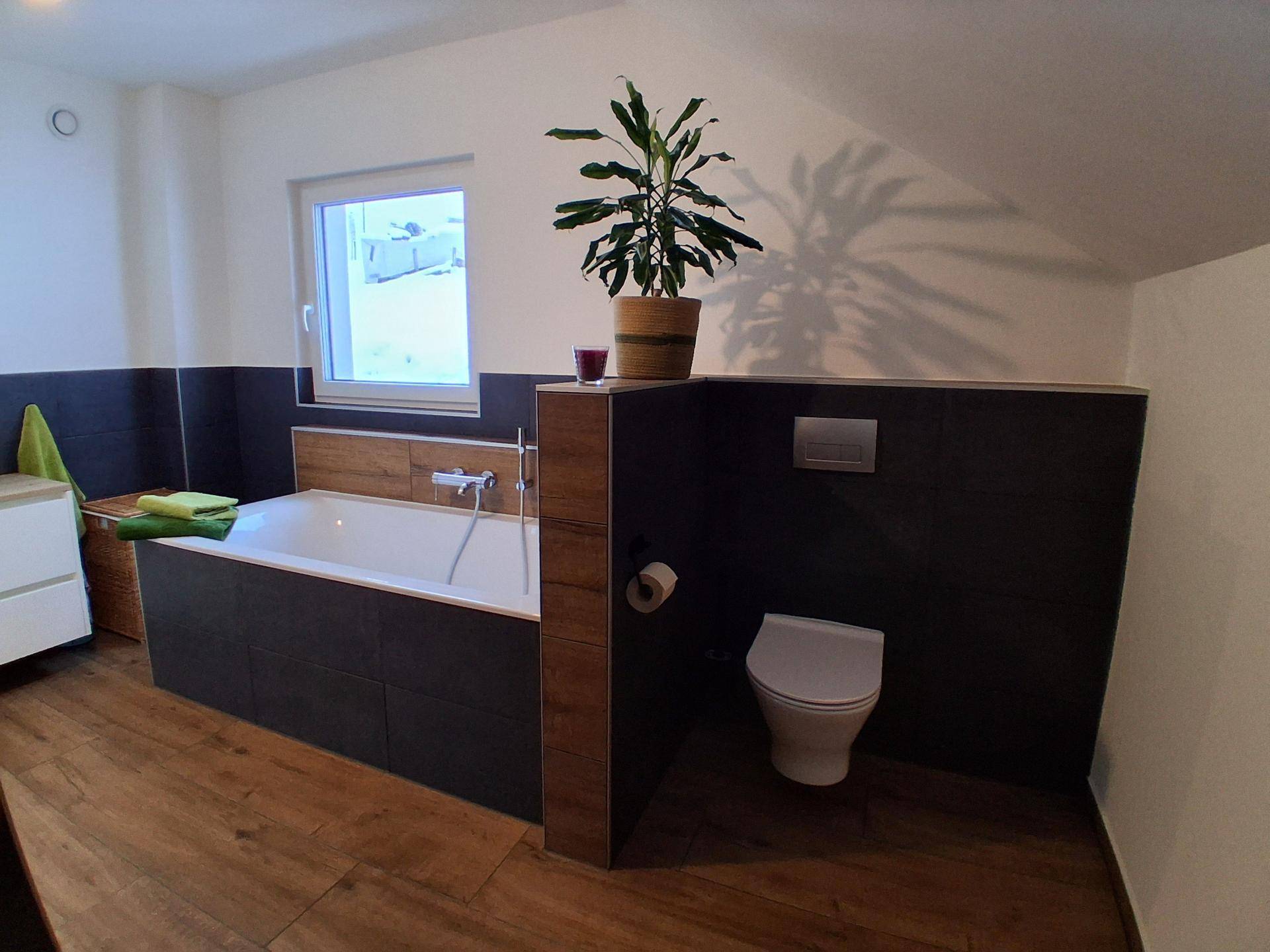 Badezimmer mit Badewanne, wandhängendem WC und Fenster für natürliches Licht.