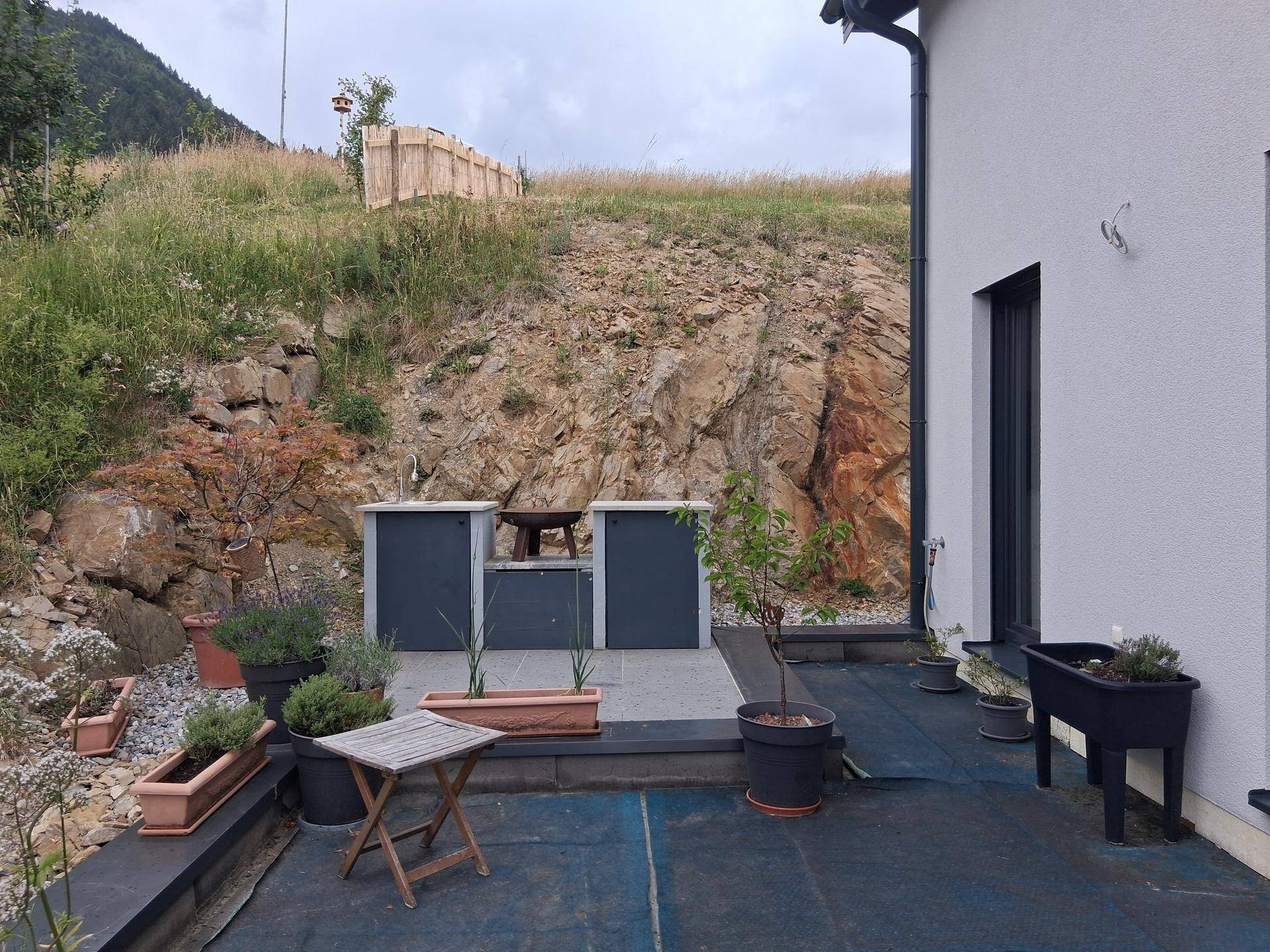 Terrasse mit Außenküchenelementen und Blick auf einen felsigen Hang.