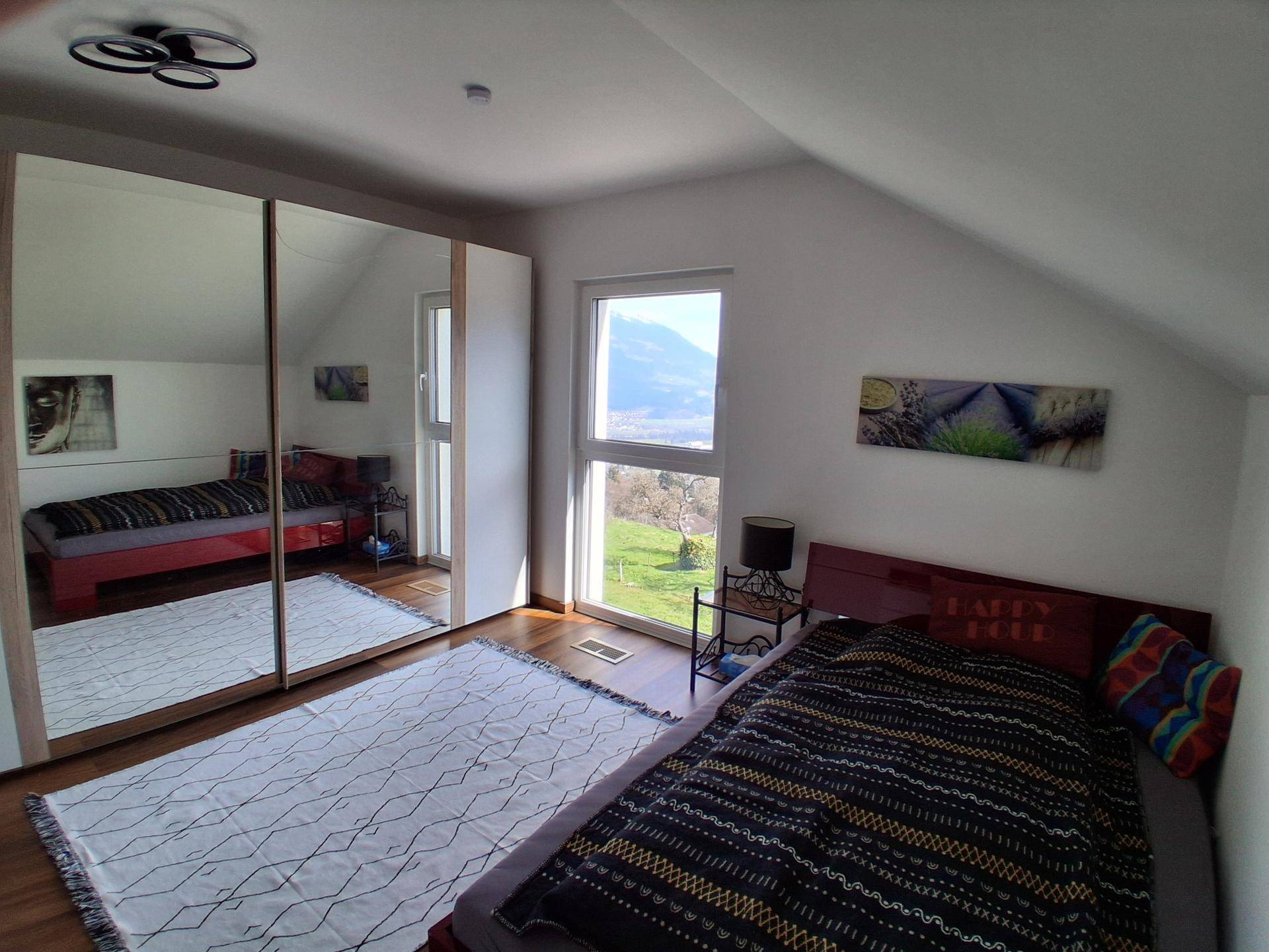Helles Schlafzimmer mit Spiegelschrank, Holzboden und weitem Blick auf die Landschaft.