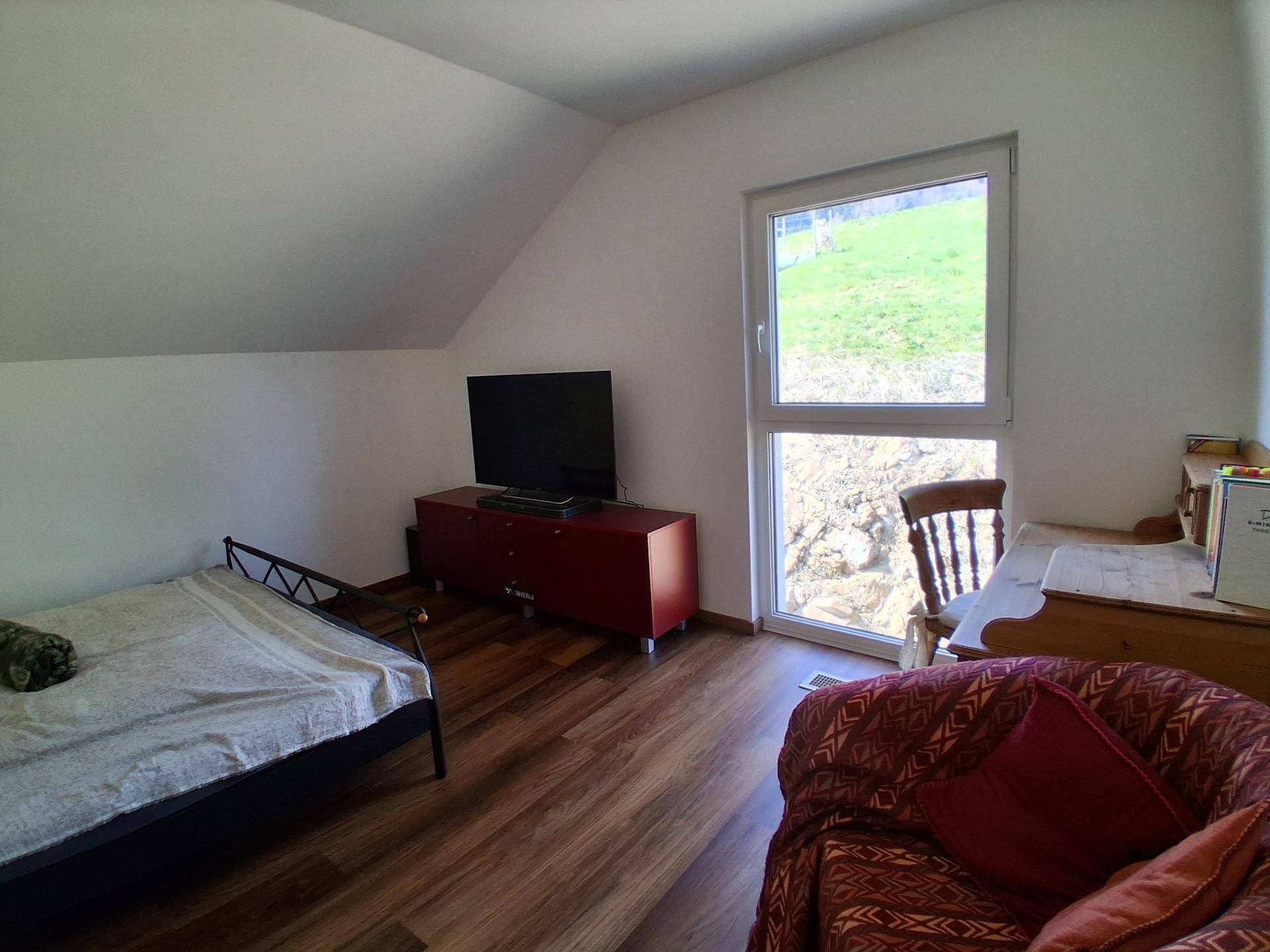 Schlafzimmer mit Dachschräge, Holzboden und großem Fenster mit Blick ins Grüne.