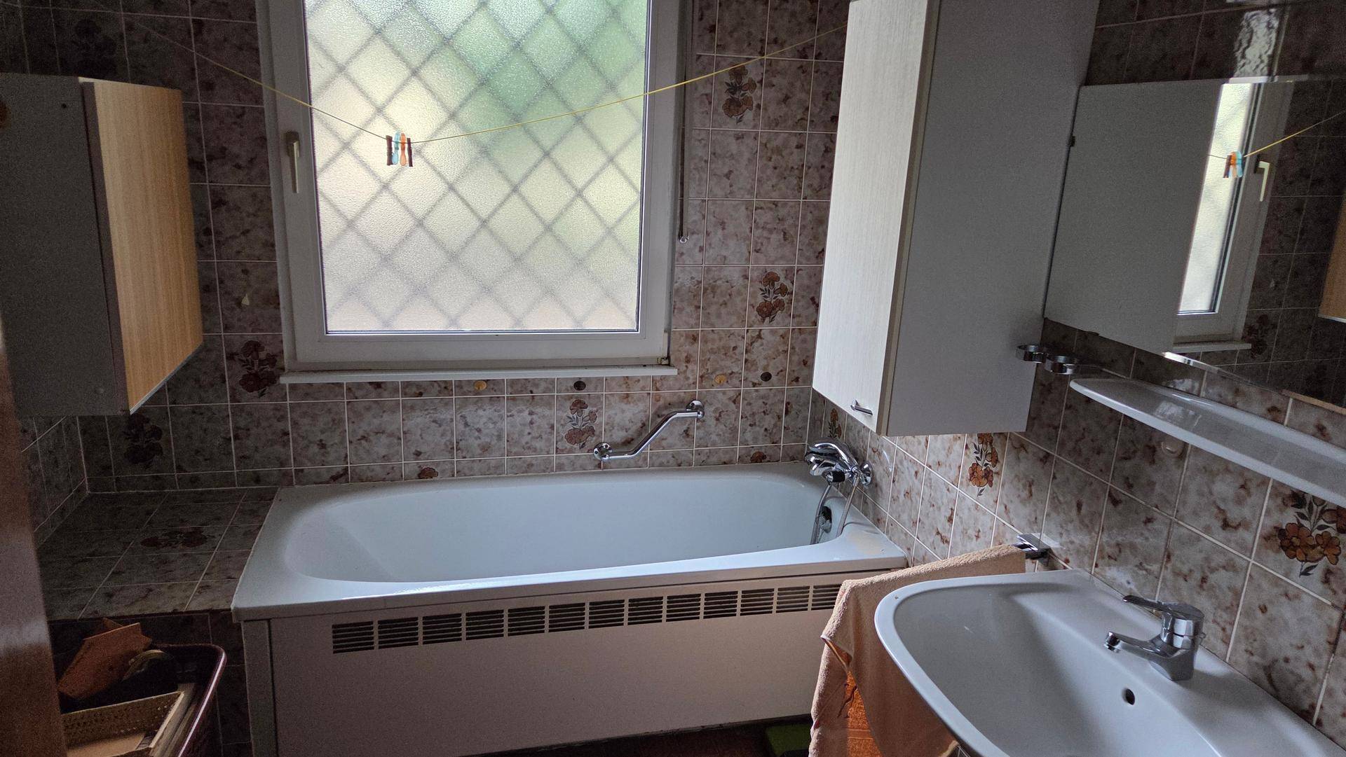 Badezimmer mit Badewanne, Waschbecken, Spiegelschrank und gemusterten Wandfliesen.