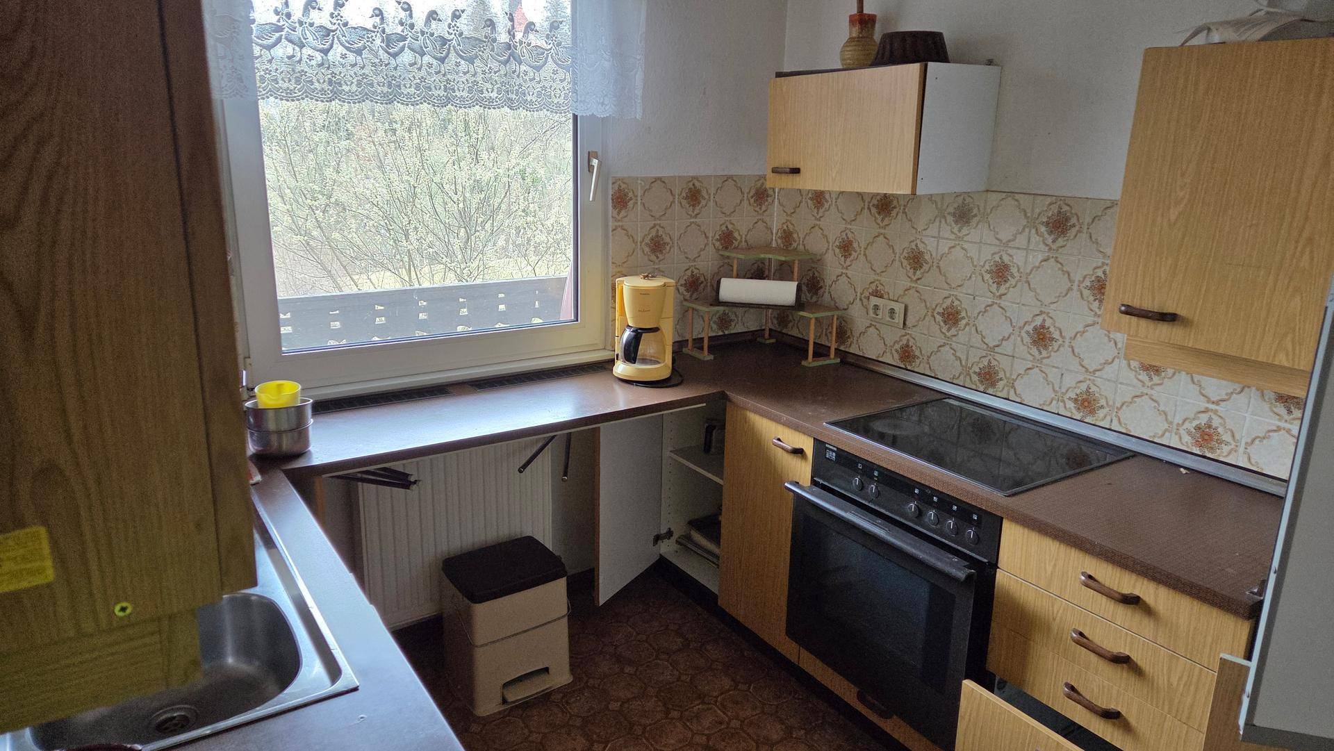 Funktionale Küche mit Holzschränken, Einbauherd, Spüle und Fenster mit Blick nach draußen.