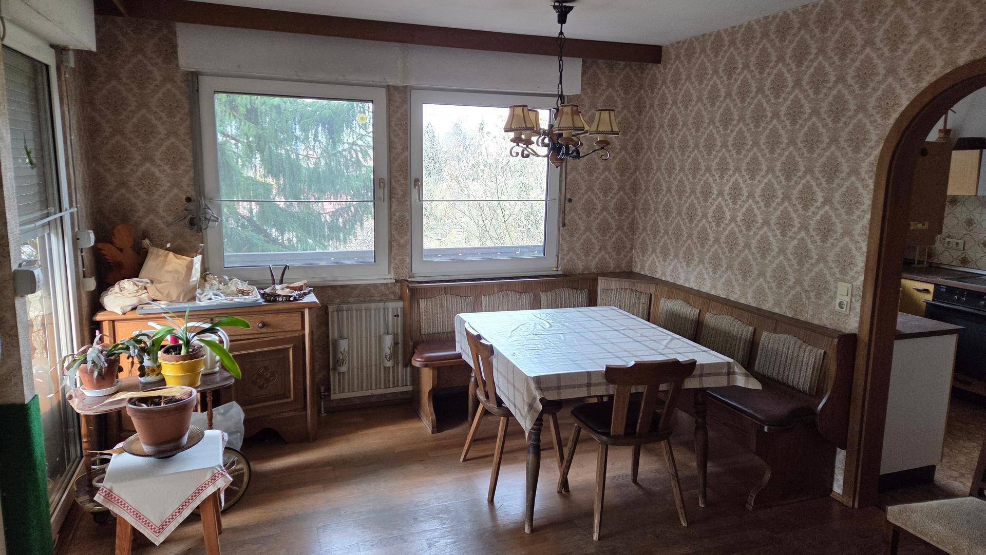 Esszimmer mit Eckbank, Holztisch, gemusterter Tapete und Blick ins Grüne.