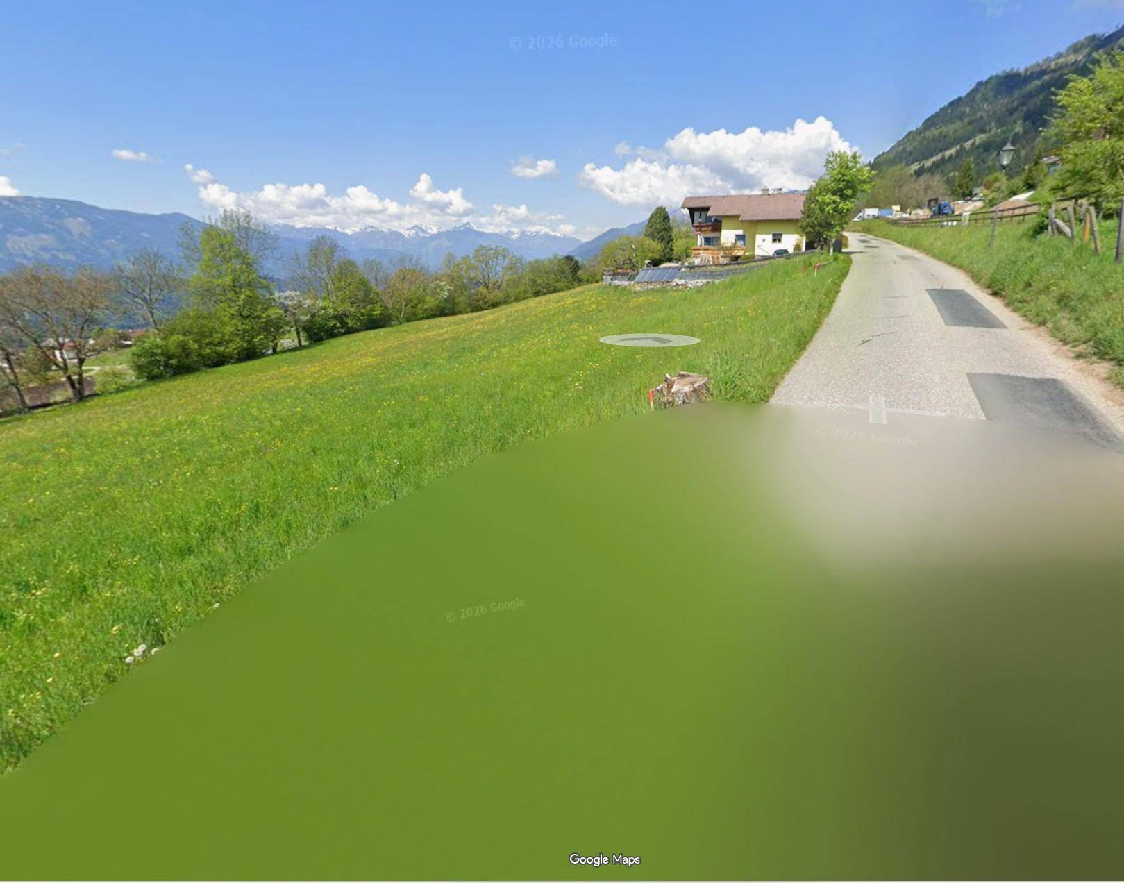 Grüne Landschaft mit einer Straße, einem Haus und majestätischen Bergen im Hintergrund.