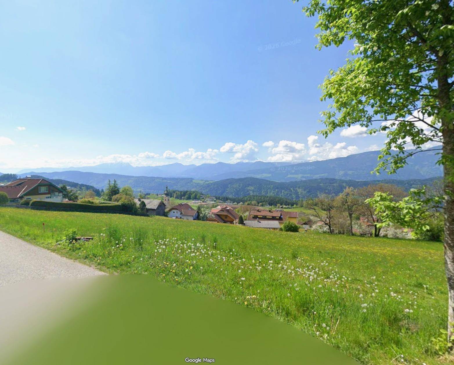 Idyllische grüne Wiese mit Blick auf eine kleine Siedlung und die beeindruckende Bergkette.