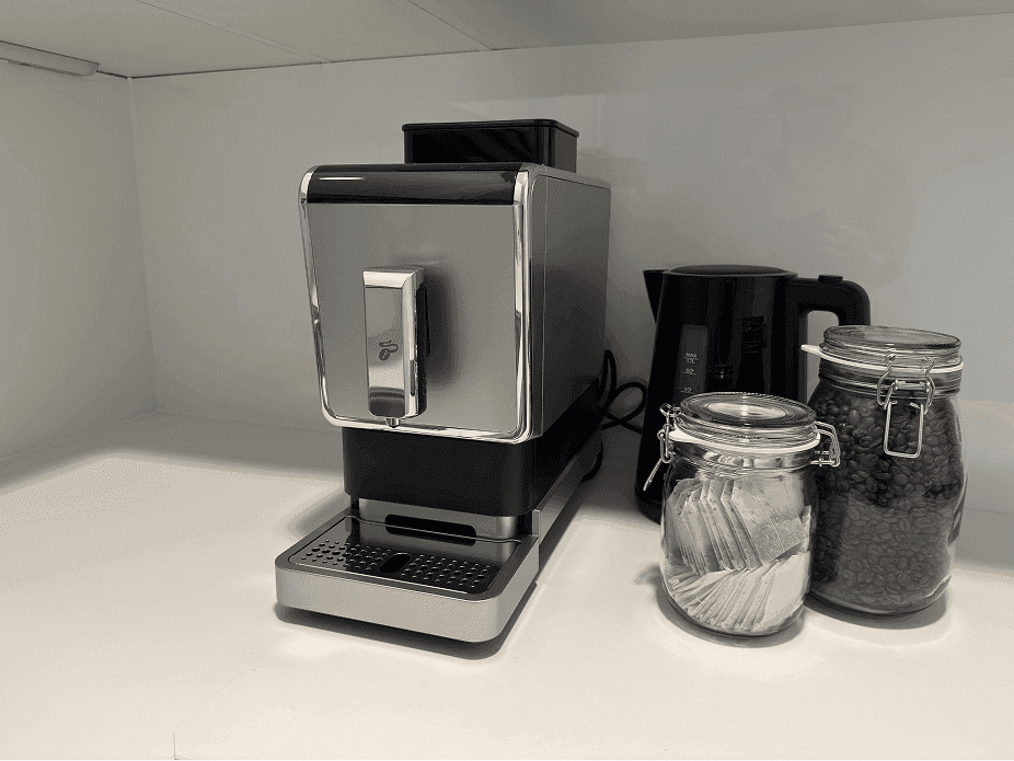 Nahaufnahme einer modernen Kaffeemaschine und Teekanne auf einer weißen Arbeitsplatte.