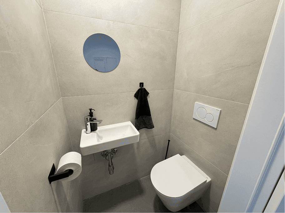 Modernes Gäste-WC mit hellgrauen Fliesen, wandhängender Toilette und kleinem Waschbecken.