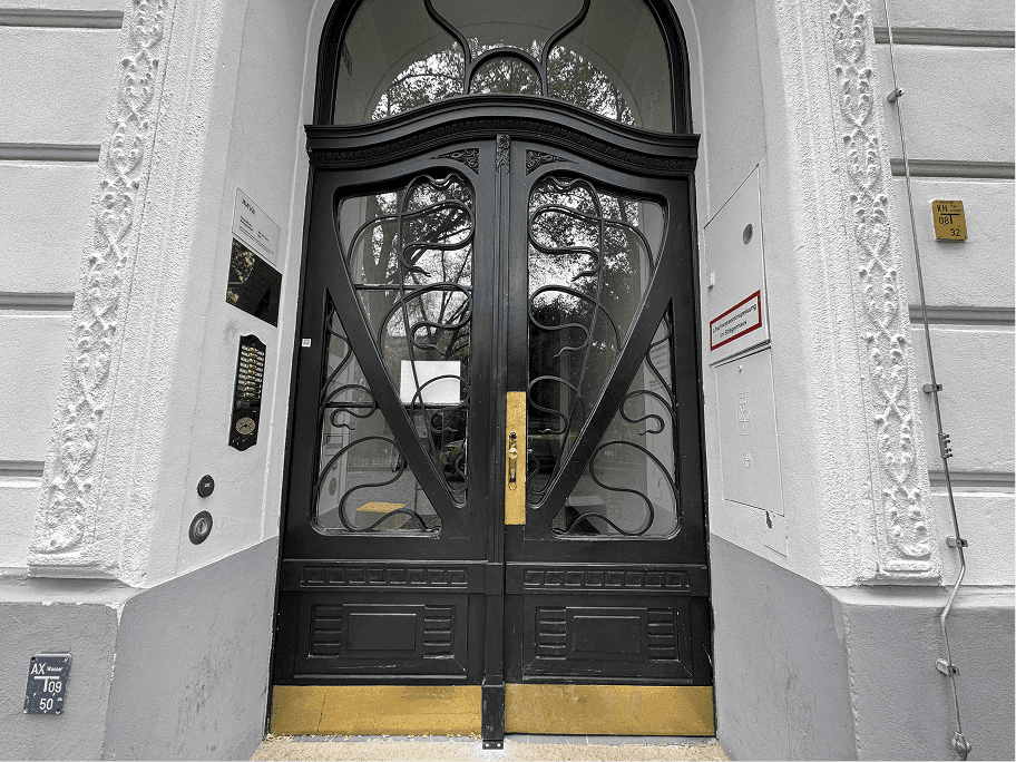 Historische, kunstvoll verzierte Eingangstür in Schwarz mit goldenen Akzenten und Stuckfassade.