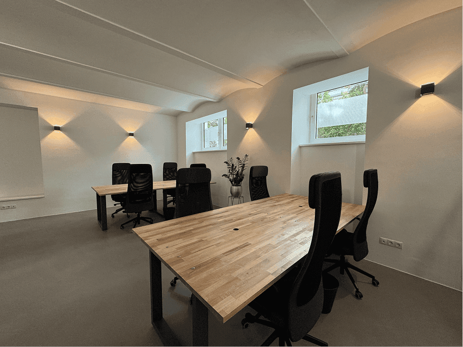 Heller Büroraum mit modernen Holzschreibtischen, ergonomischen Stühlen und Wandbeleuchtung.