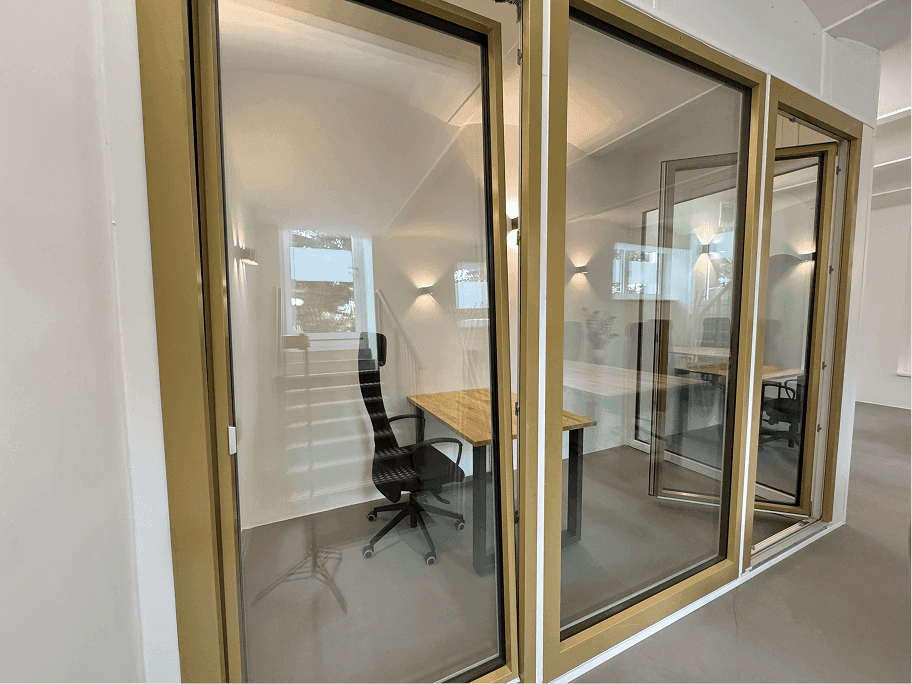 Blick durch goldgerahmte Glaswände in einen hellen Büroraum mit Schreibtisch und Stuhl.
