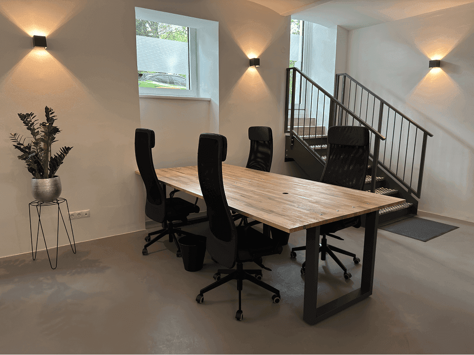 Geräumiger Bürobereich mit Holzschreibtischen, ergonomischen Stühlen und einer modernen Treppe.