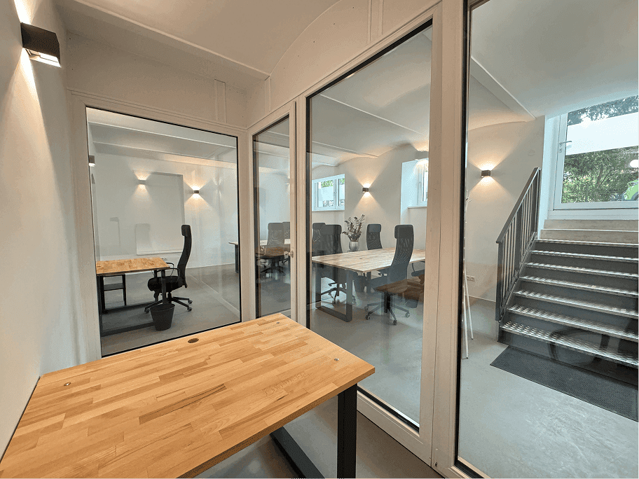 Moderner Bürobereich mit Glaswänden, Holzschreibtischen und Treppenaufgang zu weiteren Etagen.