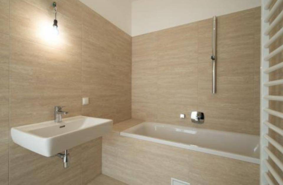 Modernes Badezimmer mit beigefarbenen Fliesen, Badewanne, Einzelwaschbecken und Handtuchheizkörper.