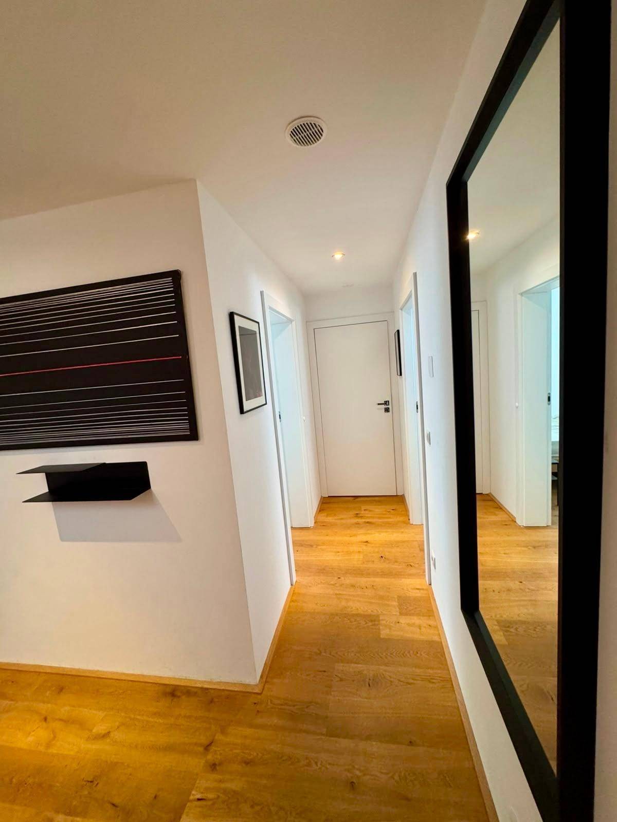 Langer, heller Flur mit Holzfußboden, großem Spiegel und minimalistischer Wanddekoration.
