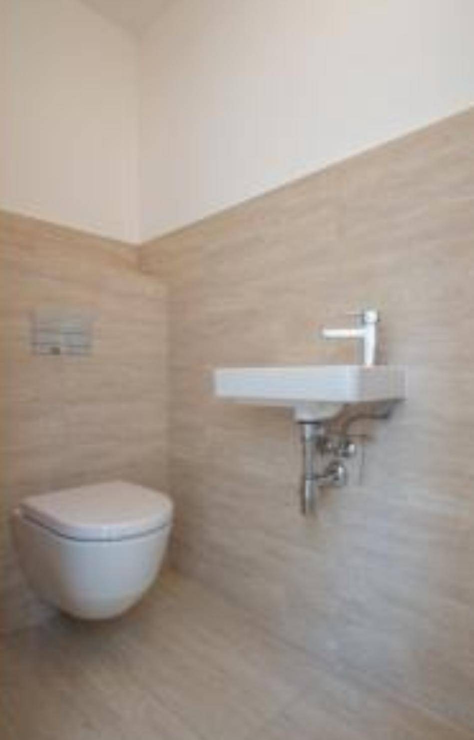 Kleines Gäste-WC mit beigefarbenen Fliesen, wandhängendem WC und Einzelwaschbecken.