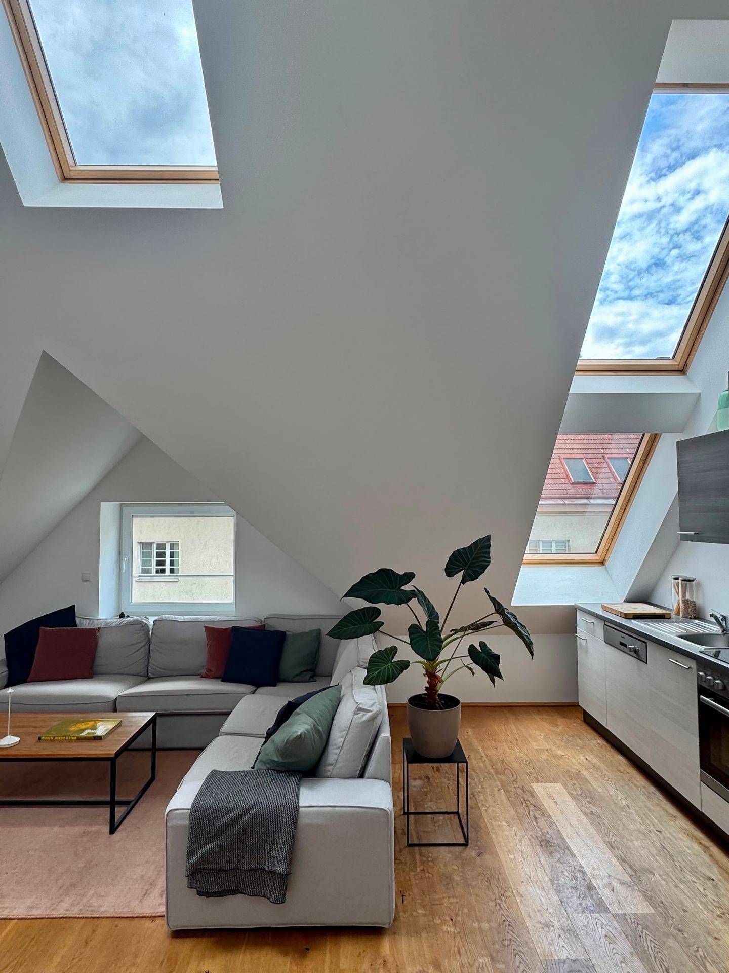 Lichtdurchfluteter Wohnbereich mit großem Ecksofa, Küchenzeile und weitem Blick durch die Dachfenster.