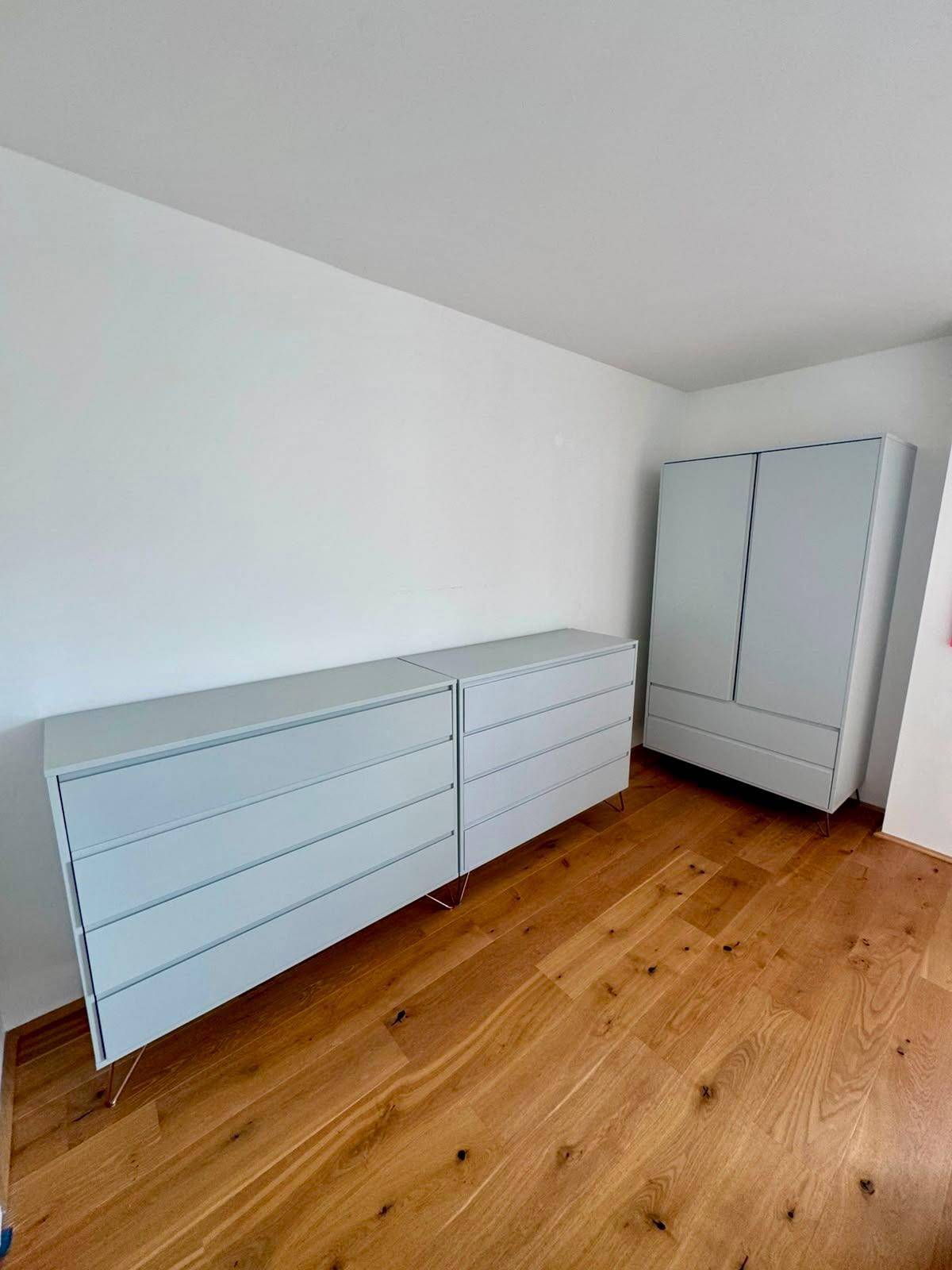 Geräumiges Schlafzimmer mit hellgrauen Kommoden, Kleiderschrank und warmem Holzfußboden.