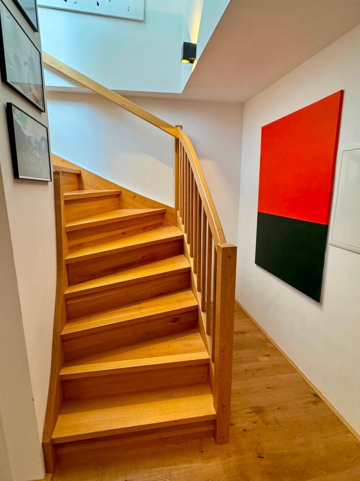 Elegante Holztreppe mit modernem Kunstwerk an der Wand und hellem Holzfußboden.