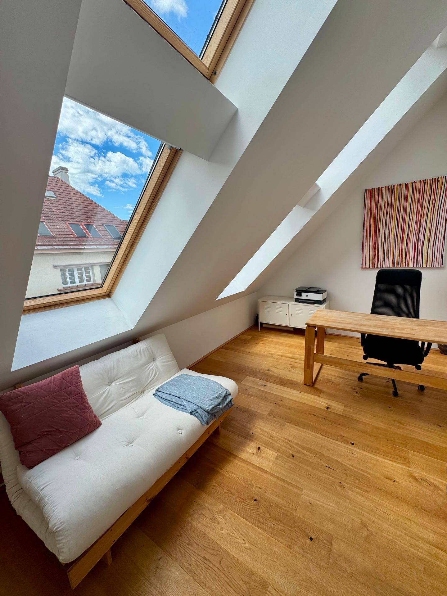 Helles Arbeitszimmer mit Schreibtisch, Tagesbett und großen Dachfenstern, die viel Licht hereinlassen.