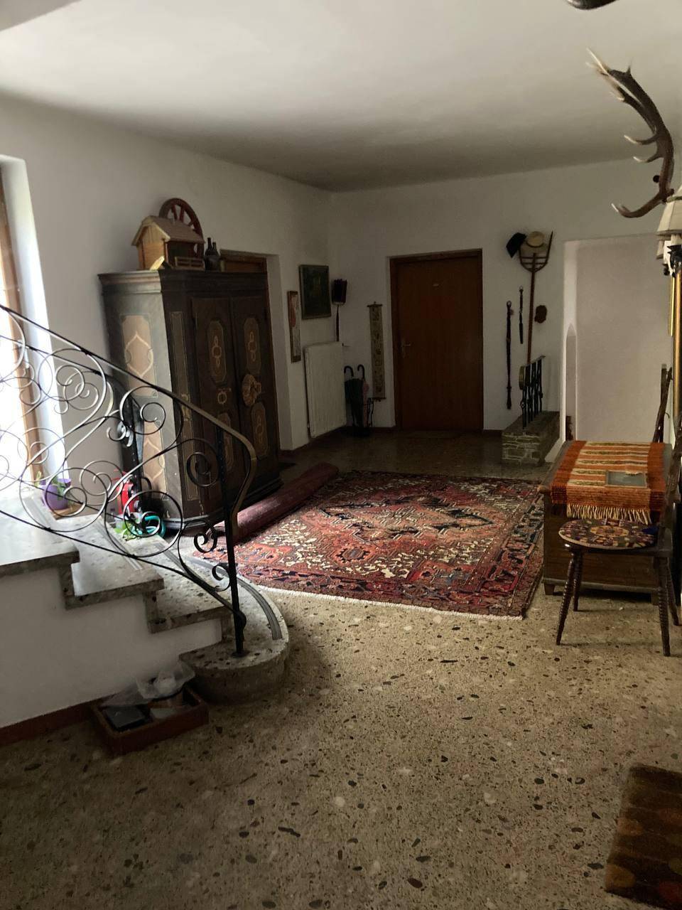Geräumiger Eingangsbereich mit traditionellem Teppich, Holzschrank und Treppenaufgang, dekoriert mit Hirschgeweihen.