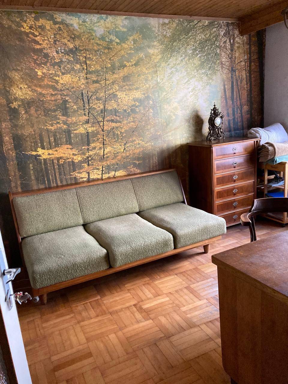 Gemütliches Wohnzimmer mit Vintage-Sofa, Holzkommode und einer Waldtapete, die eine natürliche Atmosphäre schafft.
