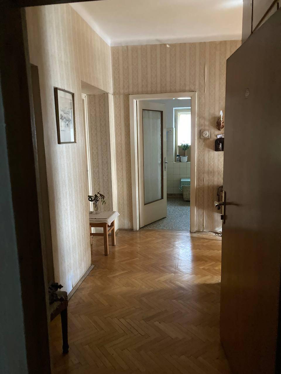 Heller Flur mit Fischgrätparkett und gestreifter Tapete, der zu weiteren Räumen führt.