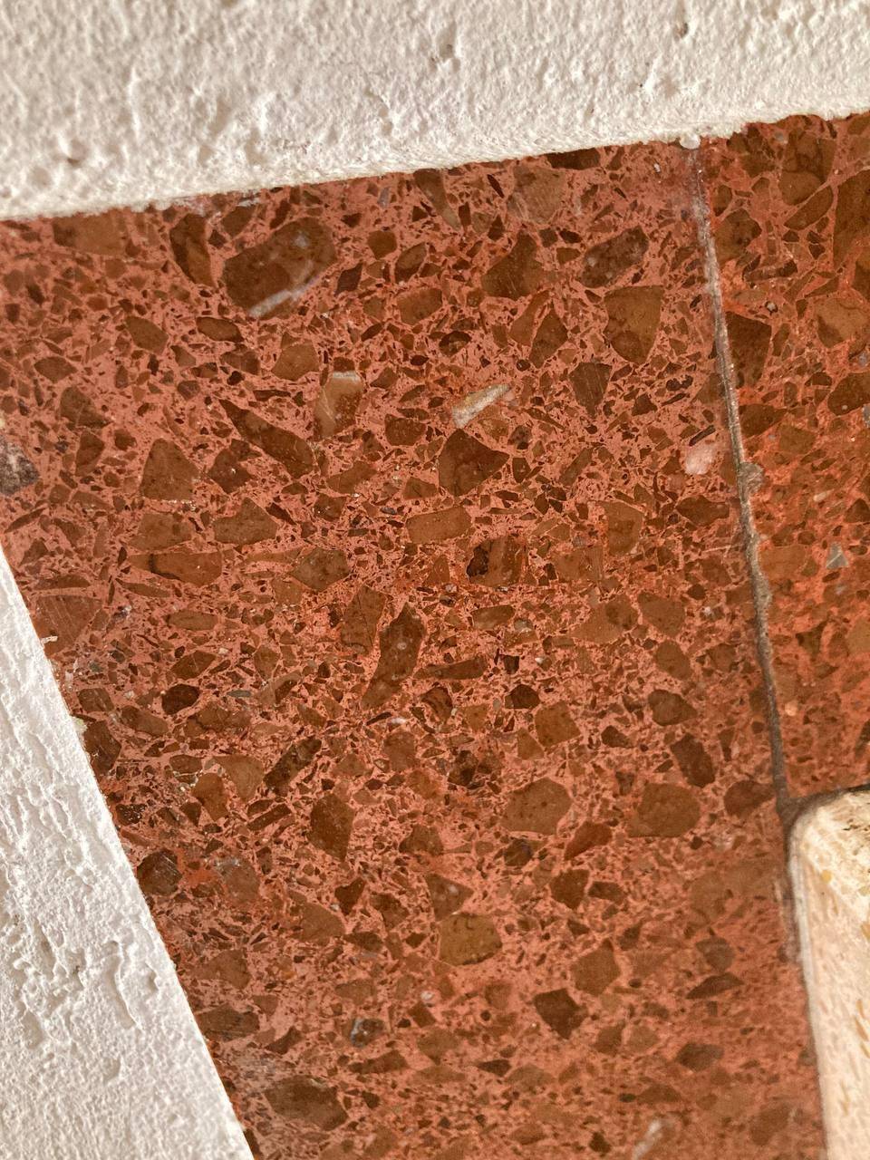 Nahaufnahme eines roten Terrazzobodens mit unregelmäßigen Steinfragmenten, die eine lebendige Textur bilden.