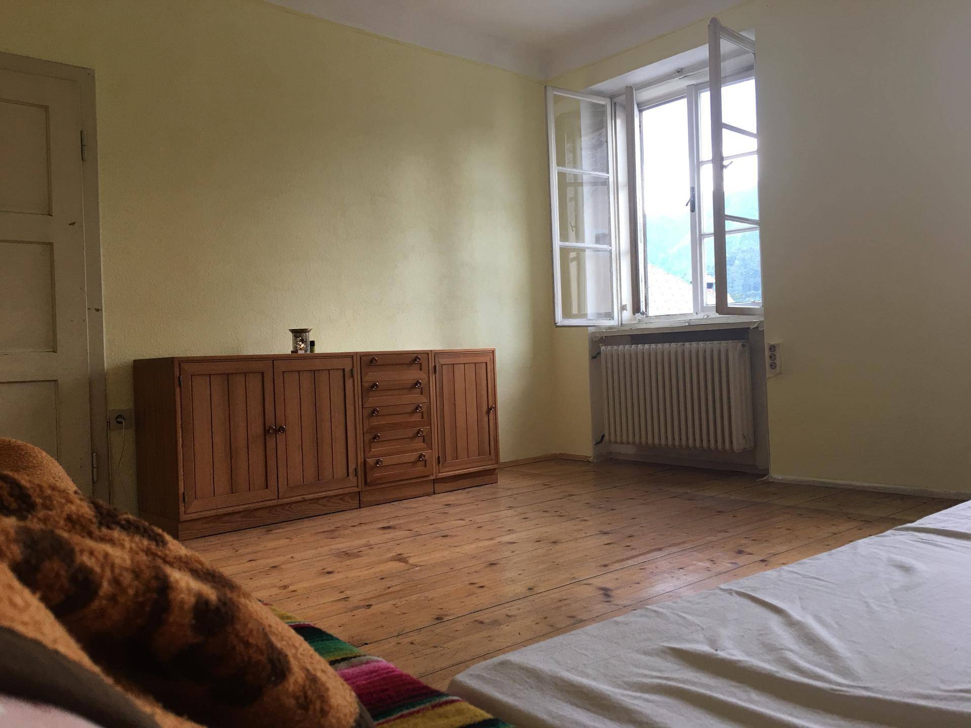 Helles Schlafzimmer mit gelben Wänden, Holzdielenboden und einem geöffneten Fenster mit Bergblick.