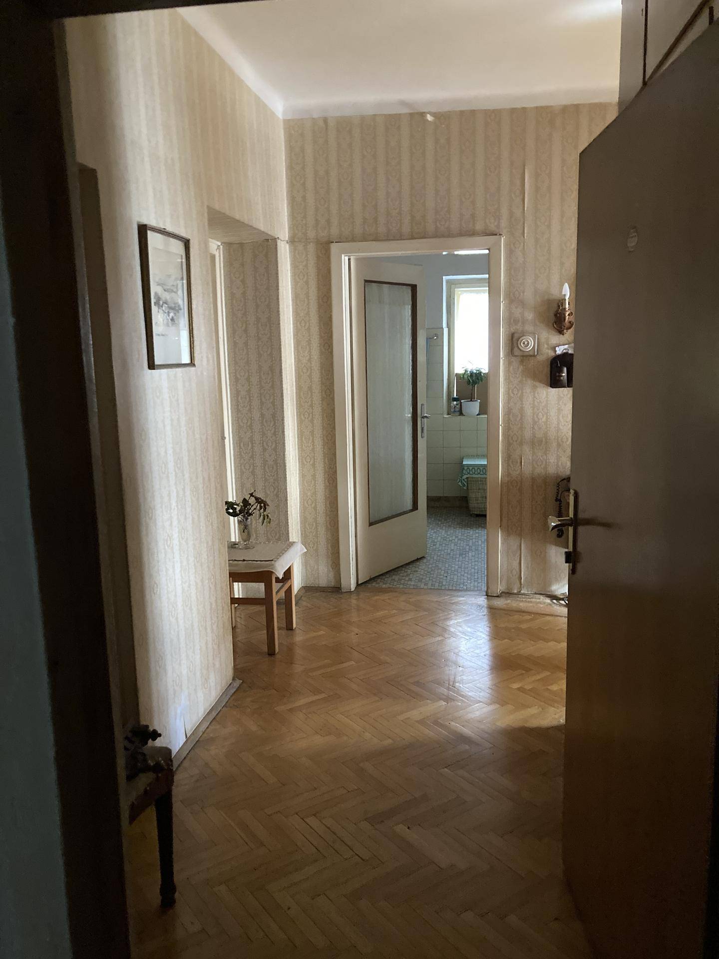 Langer Flur mit gemusterten Tapeten, Holzboden und mehreren Türen, die zu anderen Räumen führen.