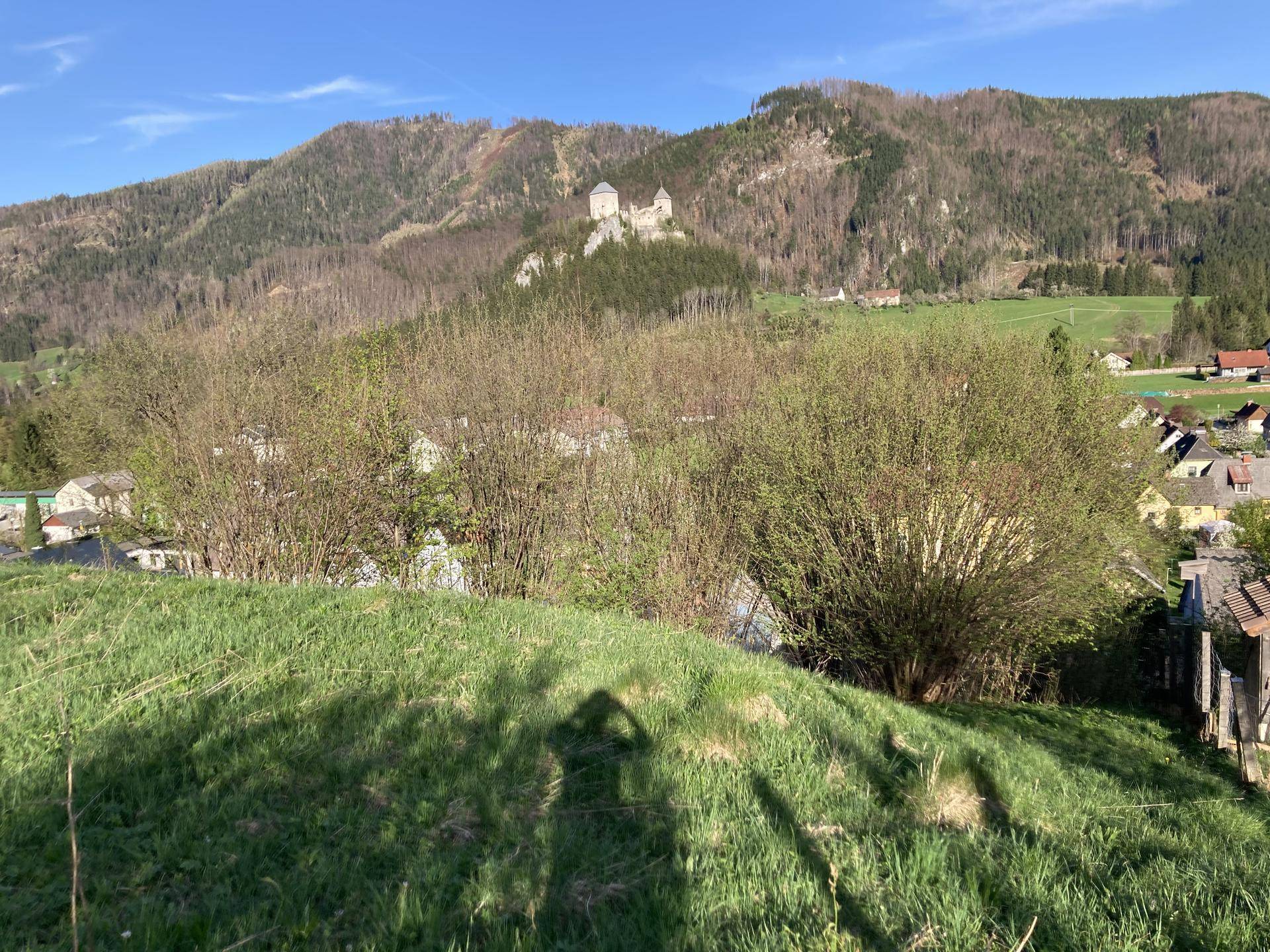 Weitläufiger Blick auf eine grüne Hügellandschaft mit einem Schloss auf einem Berg unter blauem Himmel.