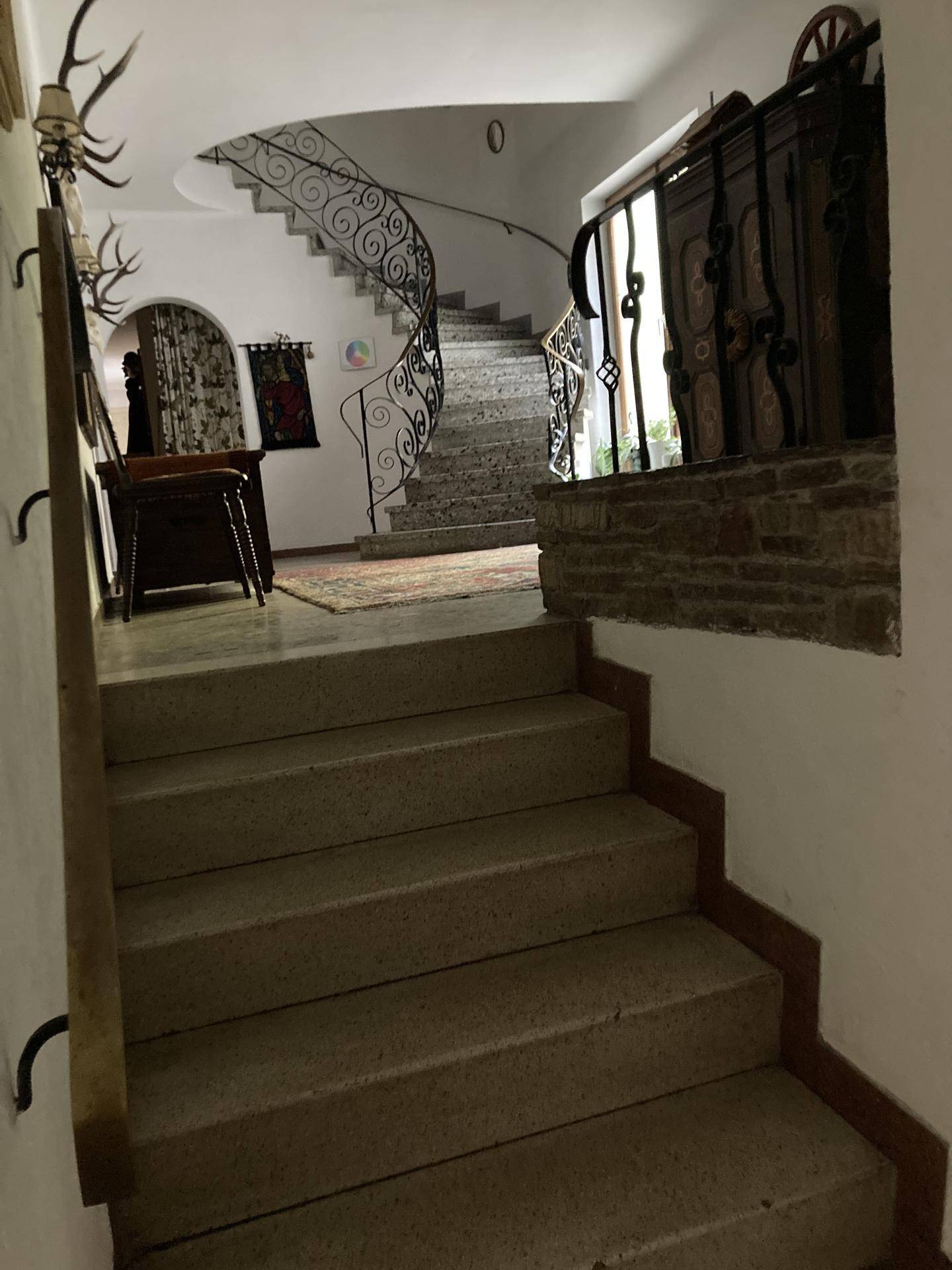 Elegantes Treppenhaus mit geschwungener Steintreppe und kunstvollem schmiedeeisernem Geländer in einem historischen Gebäude.