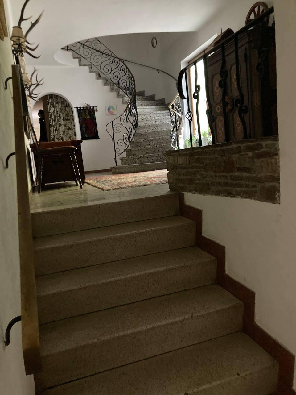 Historisches Treppenhaus mit kunstvollem schmiedeeisernem Geländer und traditionellen Hirschgeweih-Dekorationen.