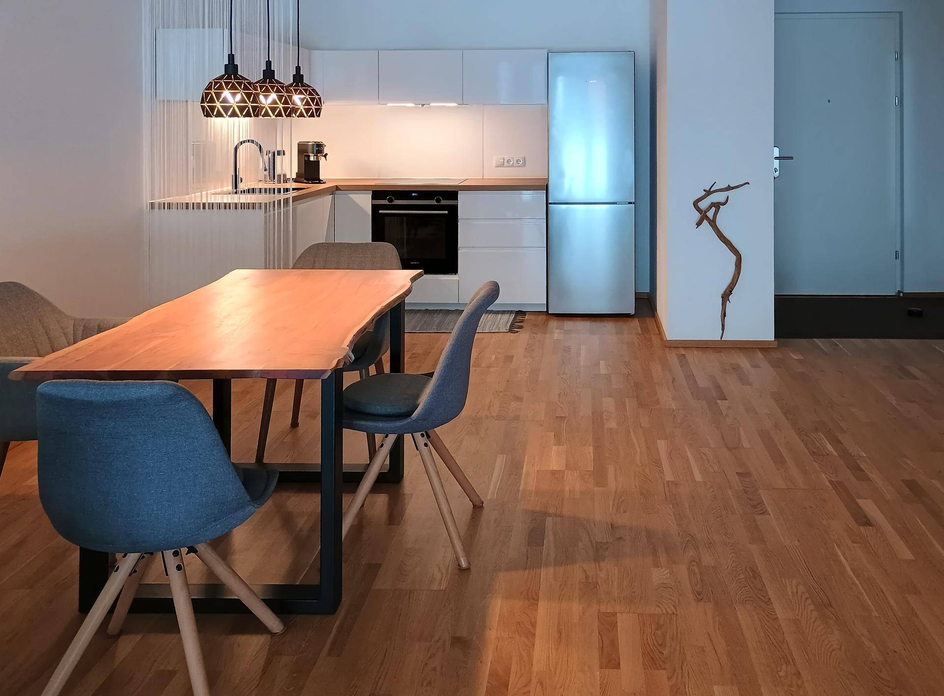 Moderne offene Küche mit weißen Hochglanzschränken, Edelstahlgeräten und Holzboden.
